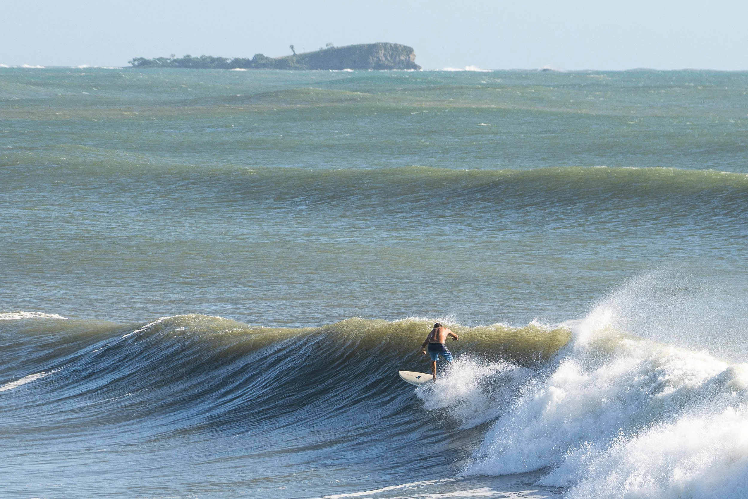 A person surfing on a wave in the ocean with a distant island visible in the background.