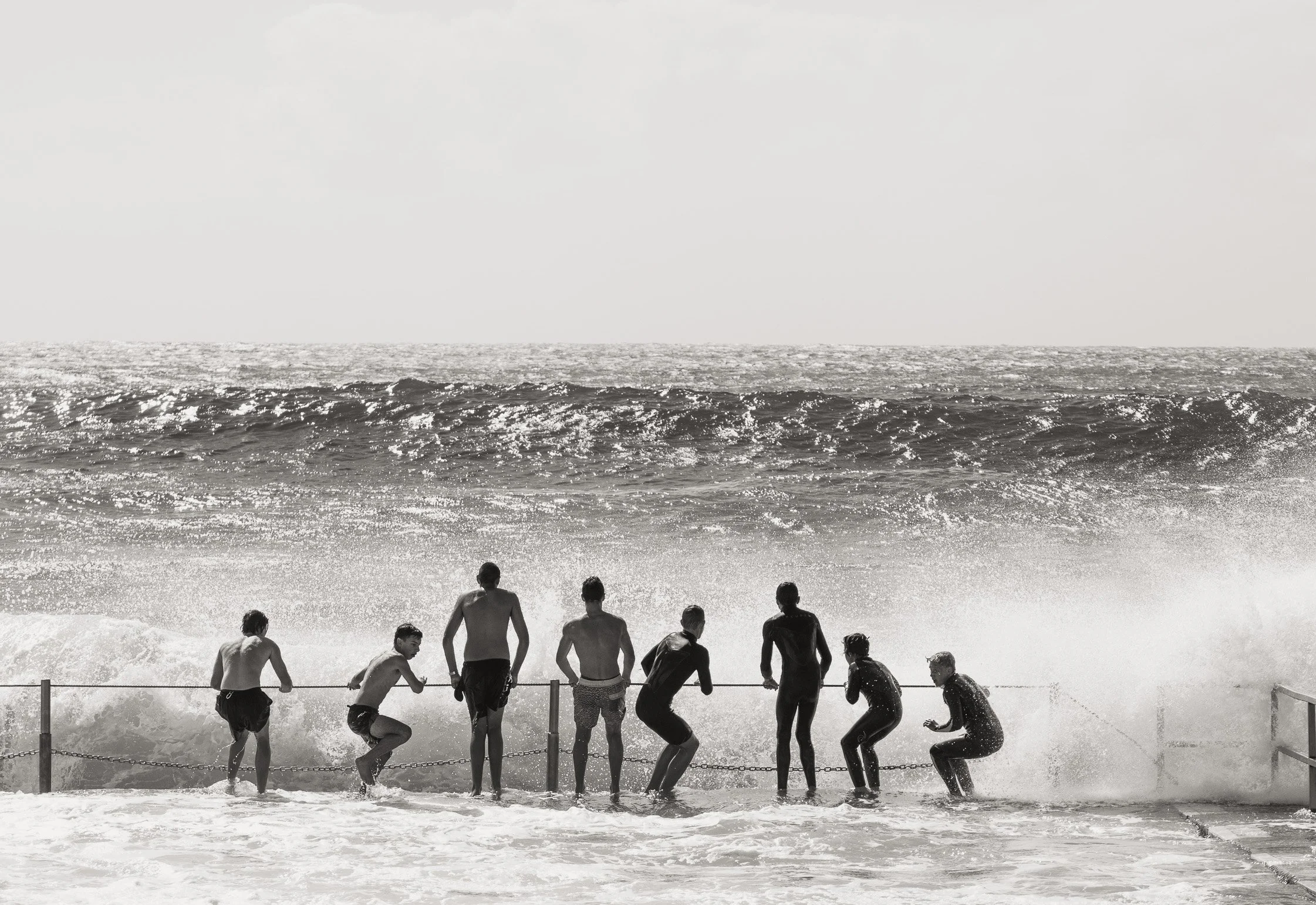Group of people standing by the ocean at the beach as waves splash on the shore, with a vast, empty sky in the background.