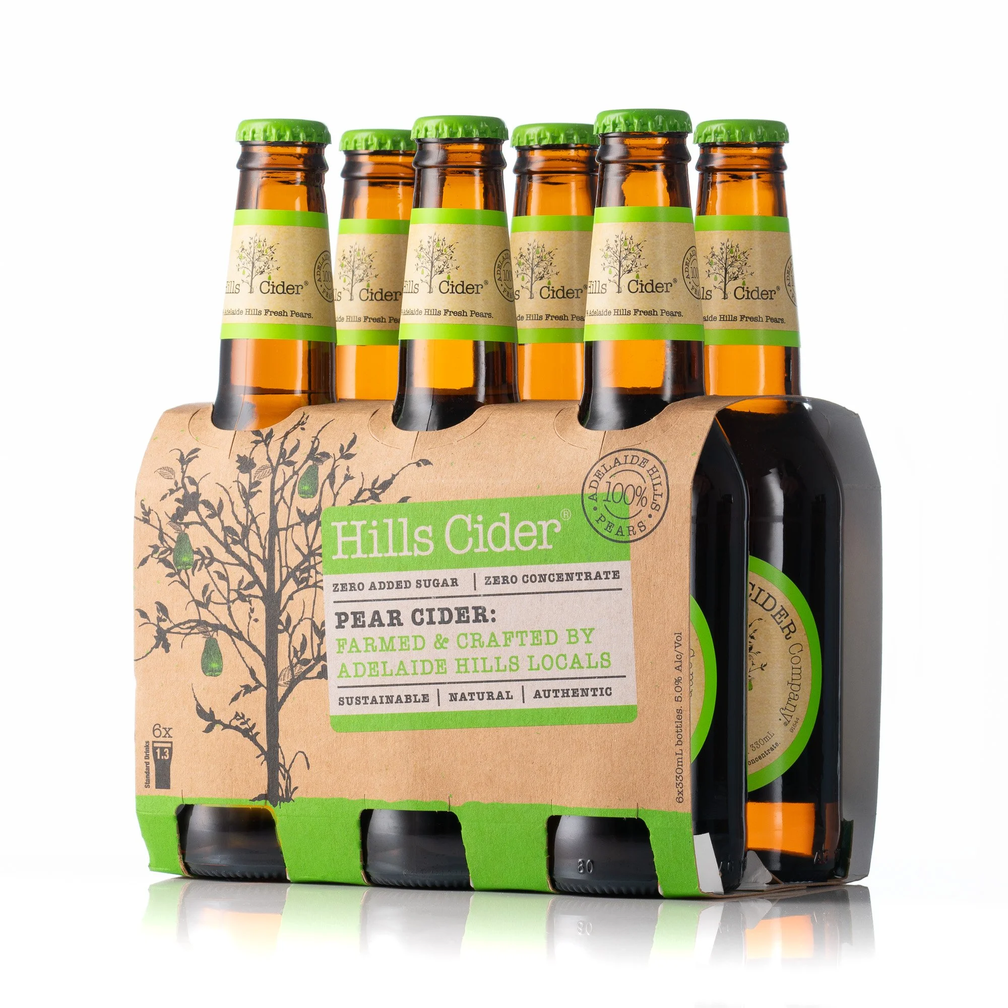 Six bottles of Hills Cider apple cider in a cardboard carrier, with lemon tree illustrations and green accents, placed on a reflective surface.