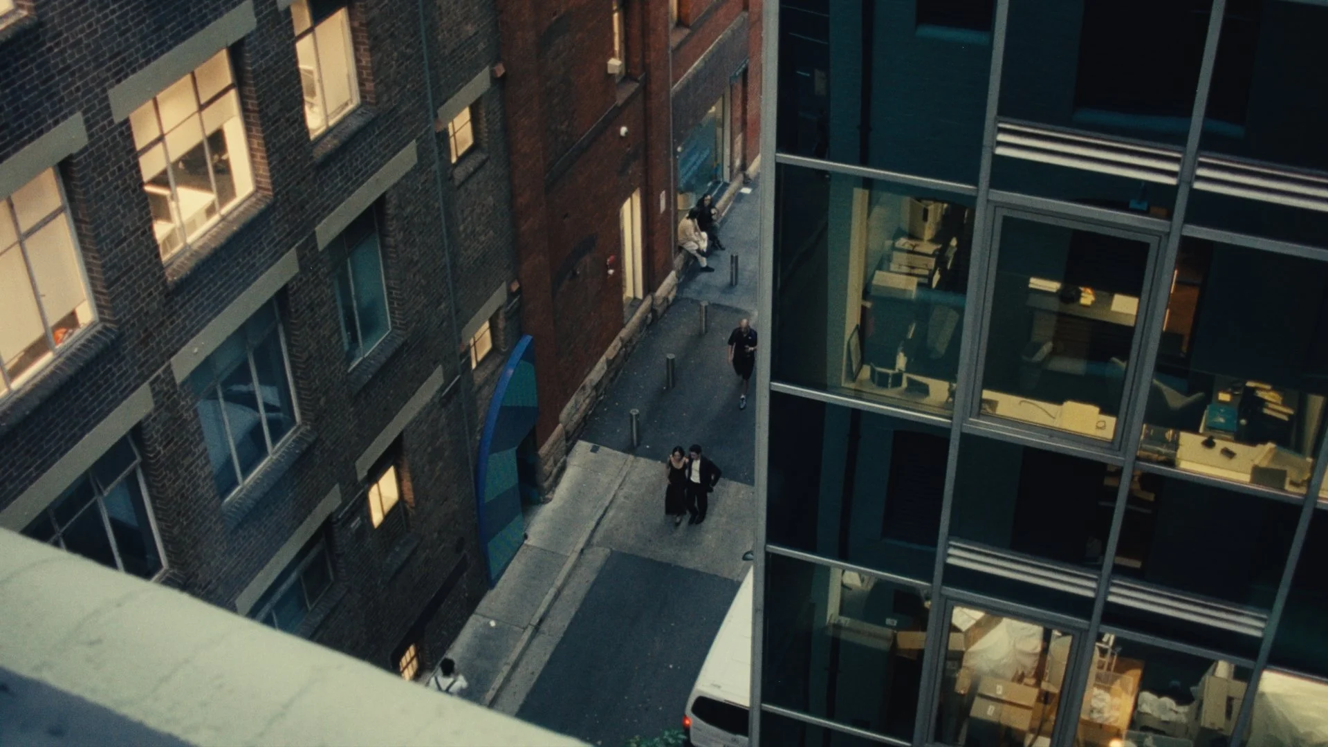 View from a high-rise building showing a city street with three pedestrians walking, surrounded by brick and glass buildings.