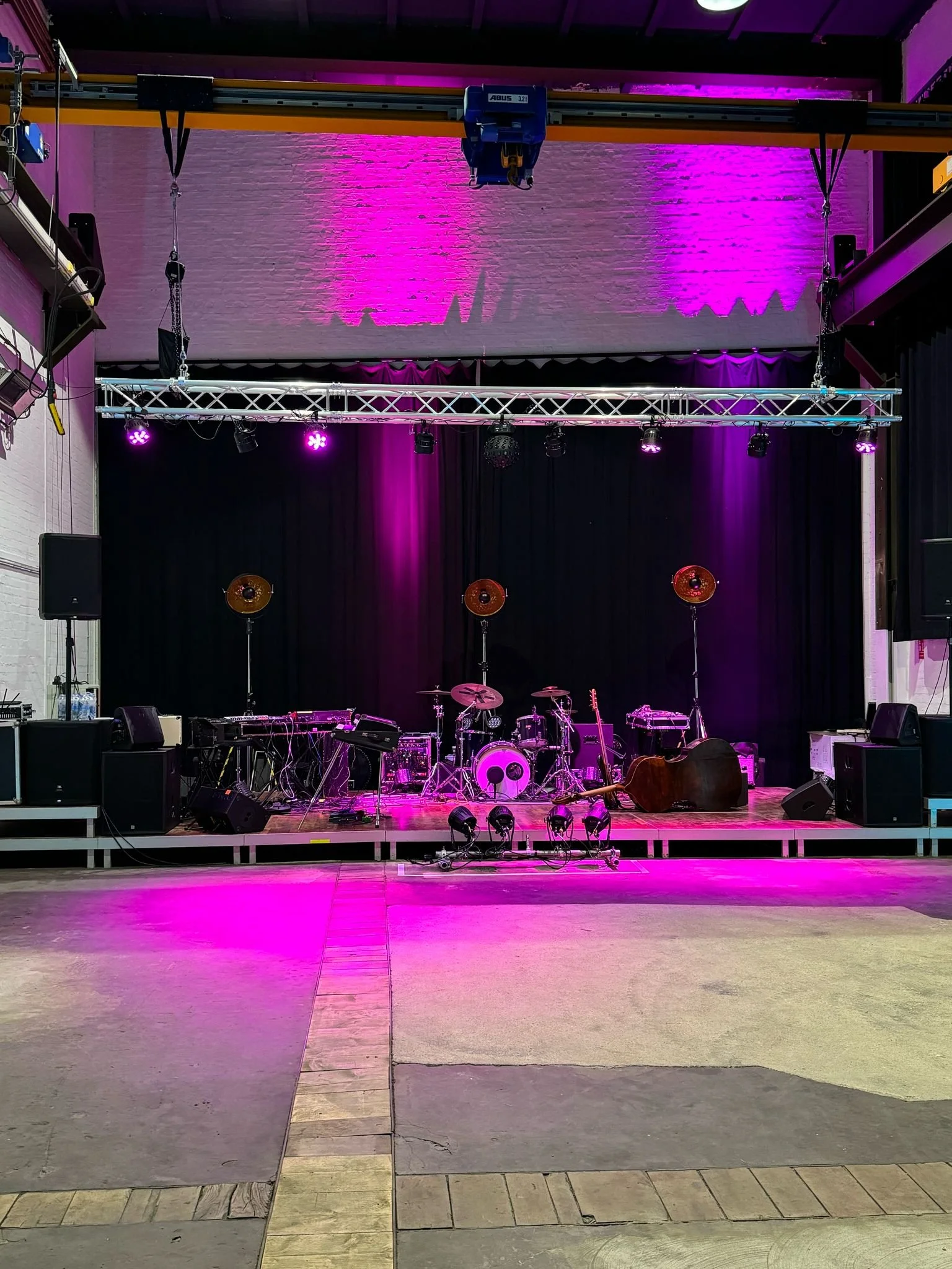 Leerer Bühnenbereich mit Musikinstrumenten, Lichttechnik und pinker Bühnenbeleuchtung in einem Veranstaltungsraum.