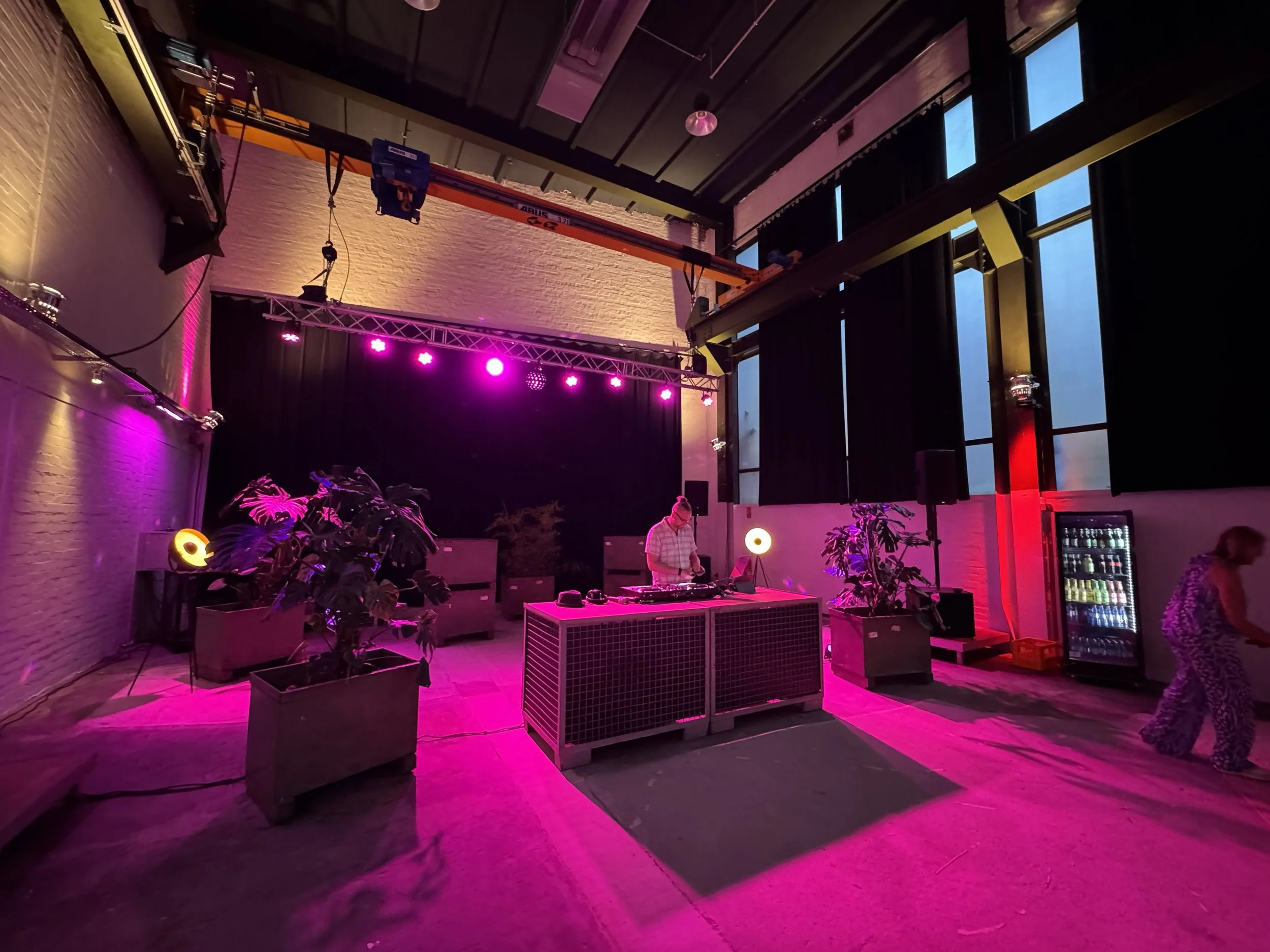 Ein Raum mit DJ-Equipment, Pflanzen, und bunten Lichteffekten, vermutlich für eine Party oder ein Event.