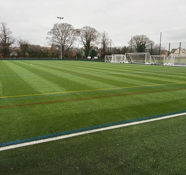 Empty soccer field with goalposts and trees in the background on a cloudy day.