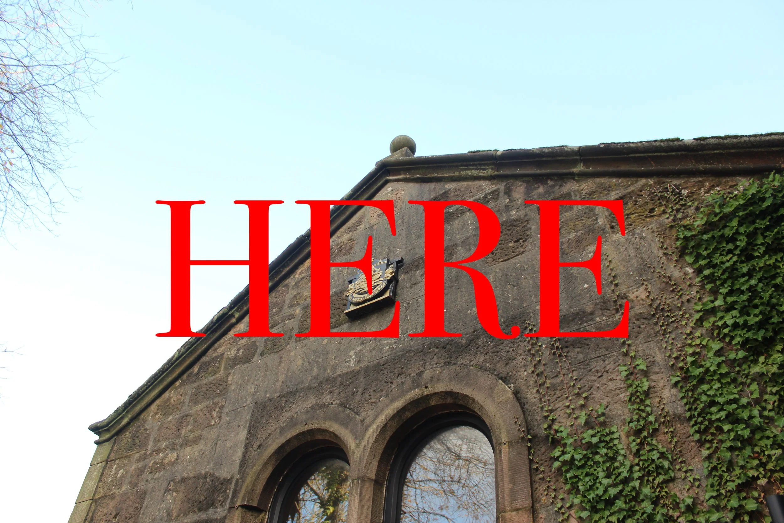 An old stone building with two arched windows and green ivy on the wall, with a large red 'HERE' text overlay.