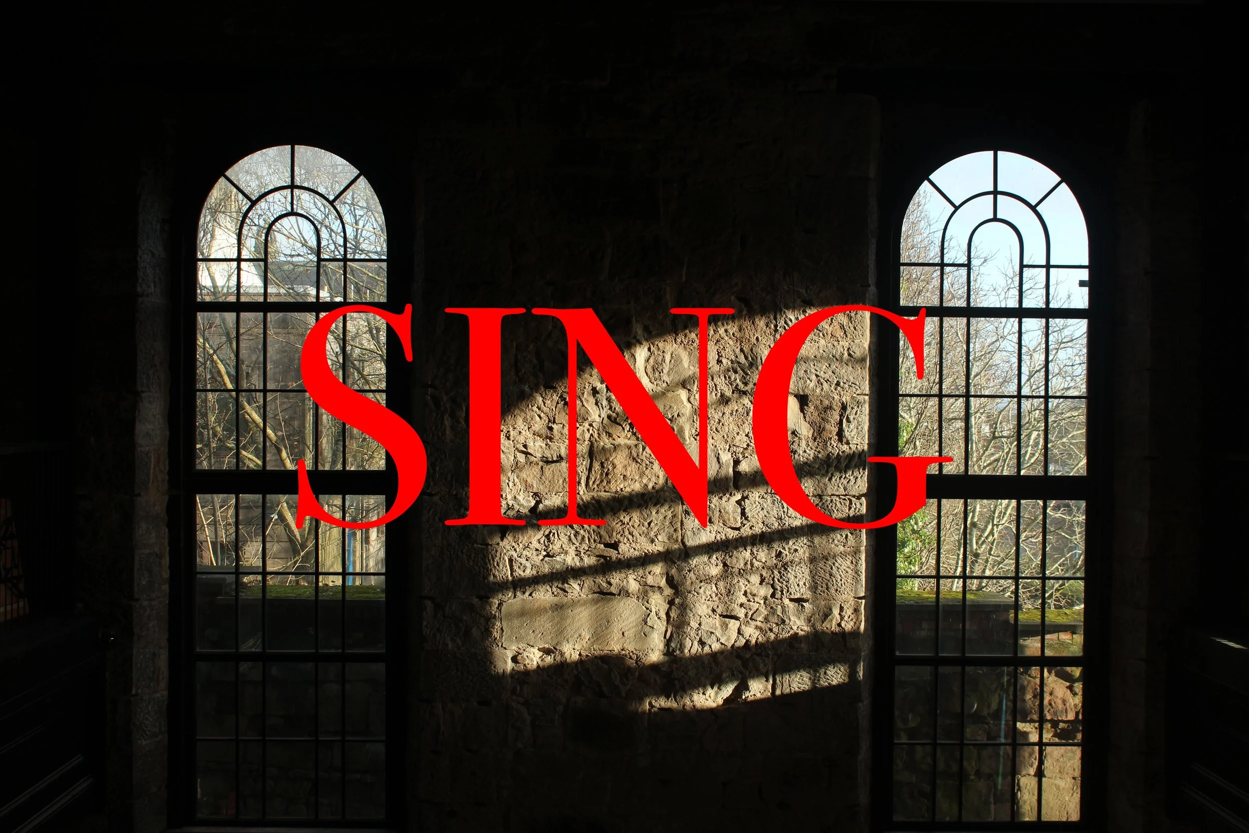 Sunlight streaming through two arched windowpanes behind a stone wall in a dark room