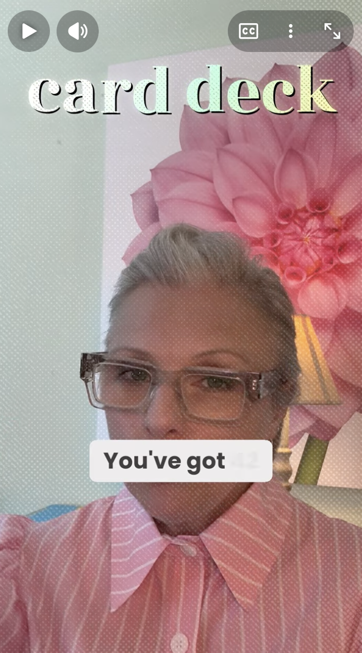 A woman with glasses and gray hair wearing a pink and white striped button-up shirt taking a selfie in front of a pink floral art piece. The image has overlay text saying 'card deck' and 'You've got'.