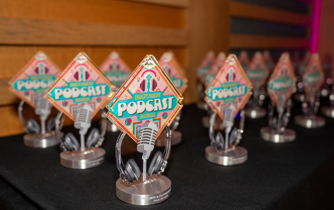 Multiple awards and trophies with podcast-themed designs and headphones on a table.