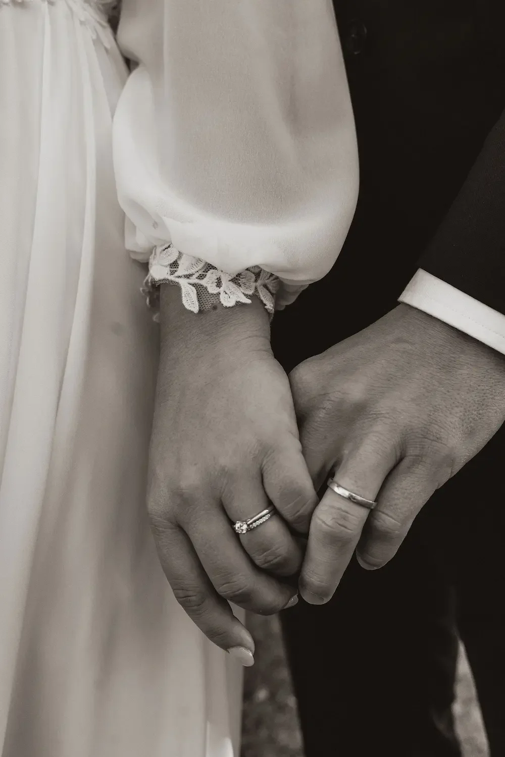 Närbild i svartvitt på brudpar som håller hand med vigselringarna i fokus. 