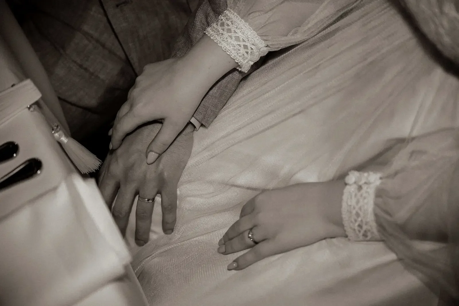 Intim närbild från ett bröllop i Malmö på brudparets händer som vilar i brudens knä.