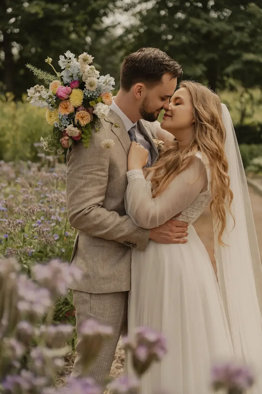 Brudpar håller om varandra i blomstrande trädgård under bröllopsfotografering på Katrinetorp Landeri i Malmö. 