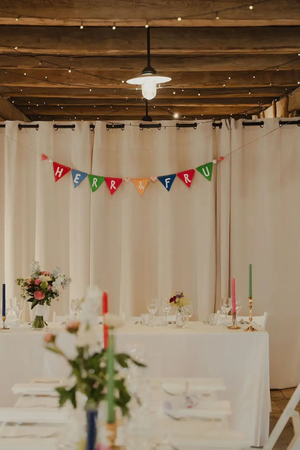 Bild på färgglada dekorationer och dukning för bröllopsmiddag i laduliknande miljö.