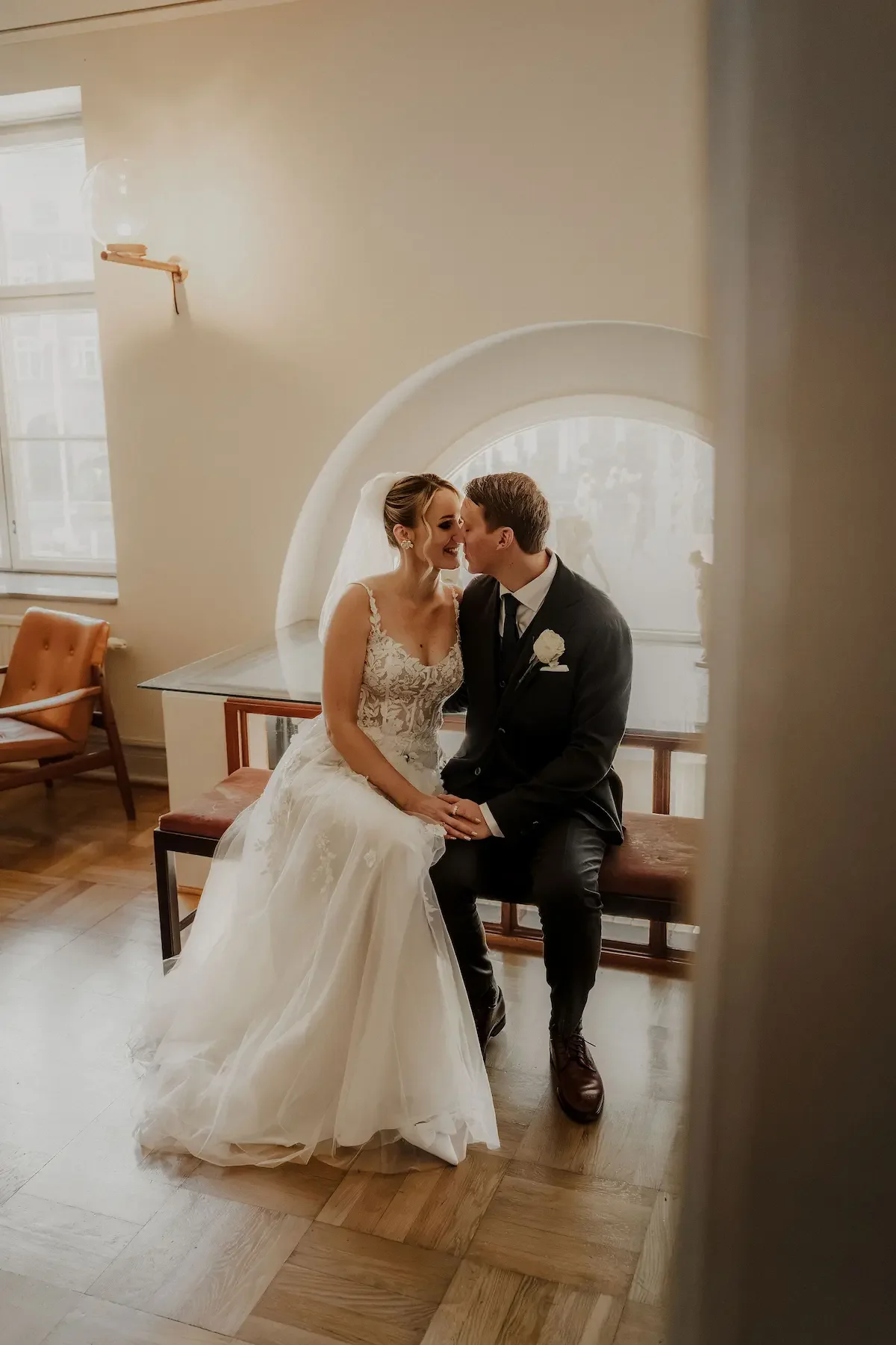 Brudpar som sitter på en bänk i Lunds rådhus och myser fångat med filmiskt, editorial känsla. 