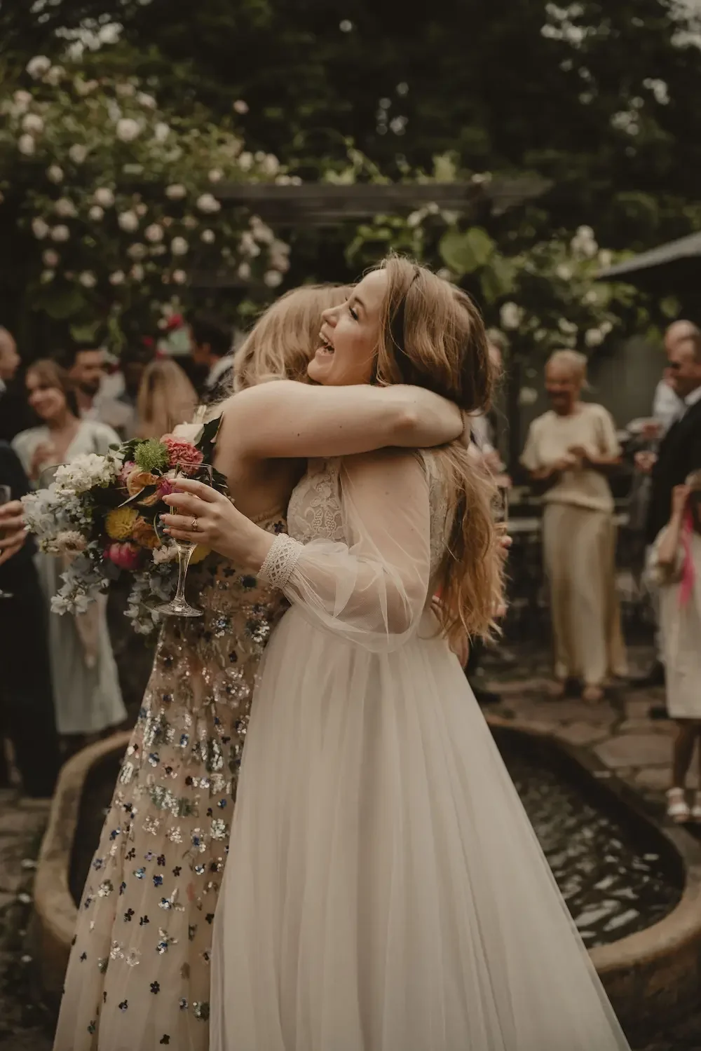 En av gästerna ger bruden en glad grattiskram under minglet i vacker trädgårdsmiljö på Katrinetorp Landeri.