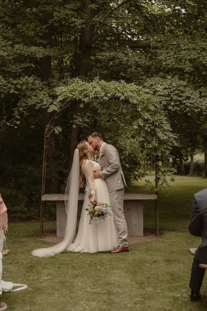 Brudpar som kysser varandra under utomhusvigsel i trädgårdsmiljö på Katrinetorp Landeri i Malmö.