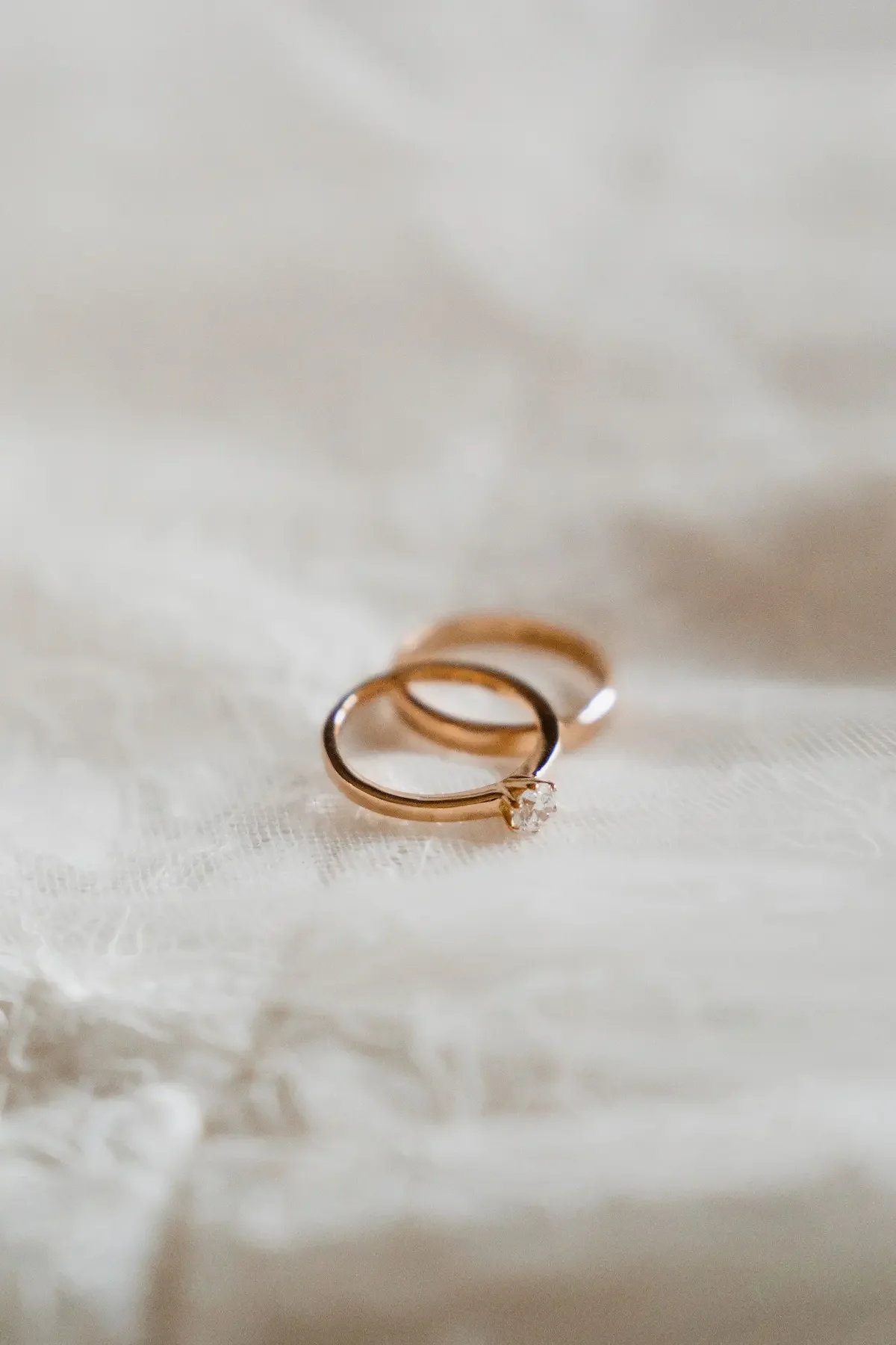 Elegant och ljus detaljbild på vigselringar som ligger ovanpå vit brudklänning. 