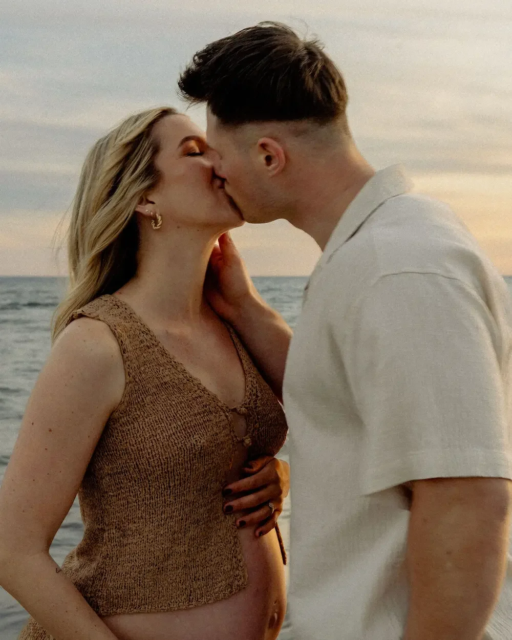 Ett par som kysser varandra i solnedgången på en strand i Skåne under en gravidfotografering.