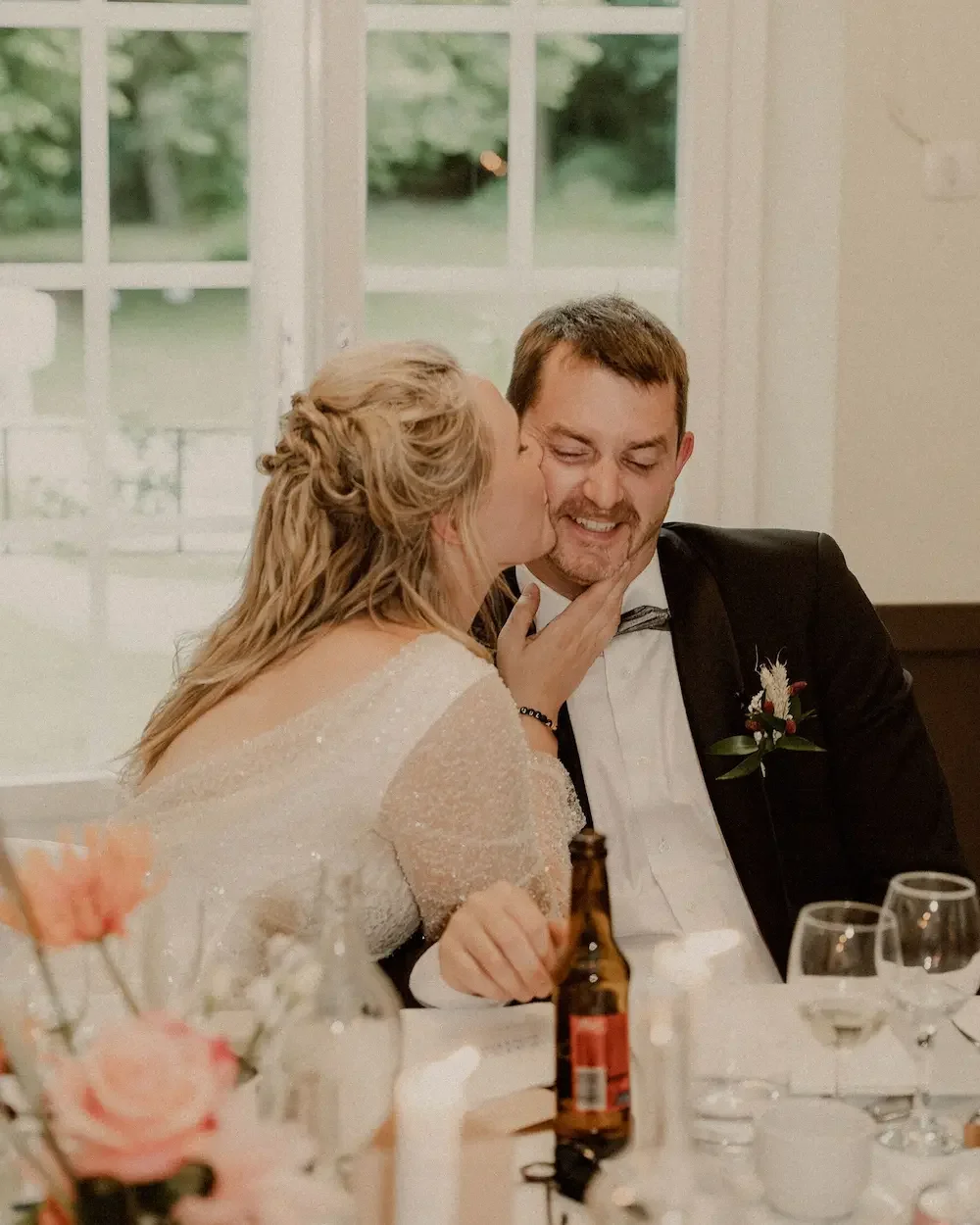 Brud kysser brudgummen på kinden under deras bröllopsmiddag i Skåne.