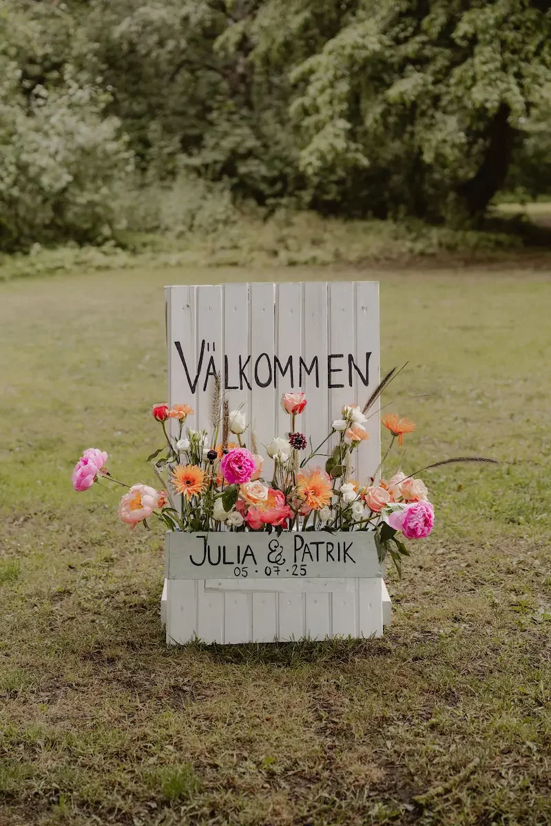 Skylt gjord av en blomlåda som hälsar gästerna välkomna till bröllopsmingel.