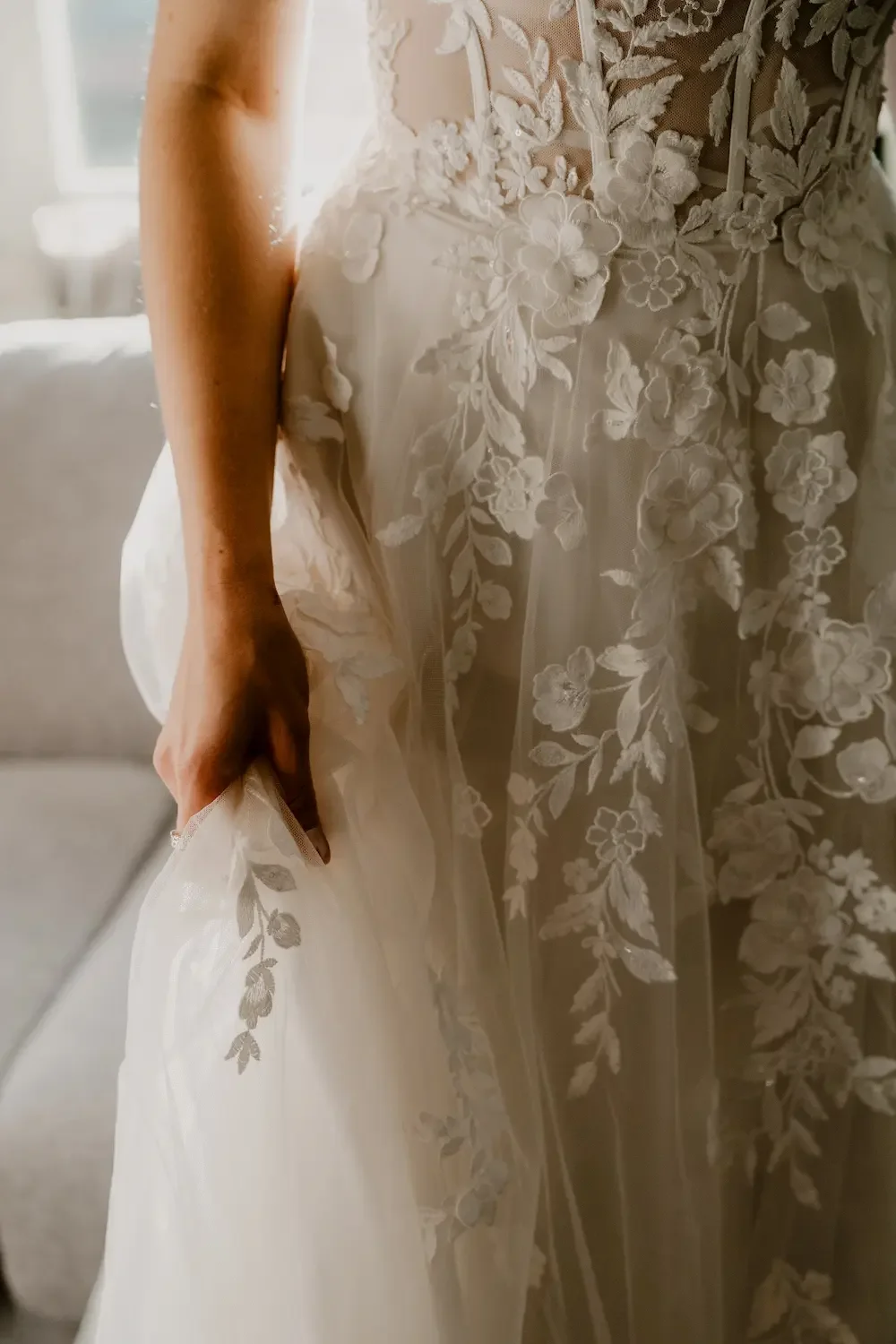 Närbild på hand och brudklänning i tyll och spets. 