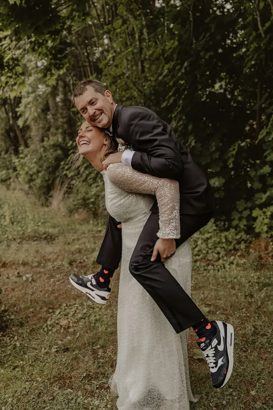 Lekfull bild på ett brudpar där bruden bär brudgummen på ryggen och skrattar. 