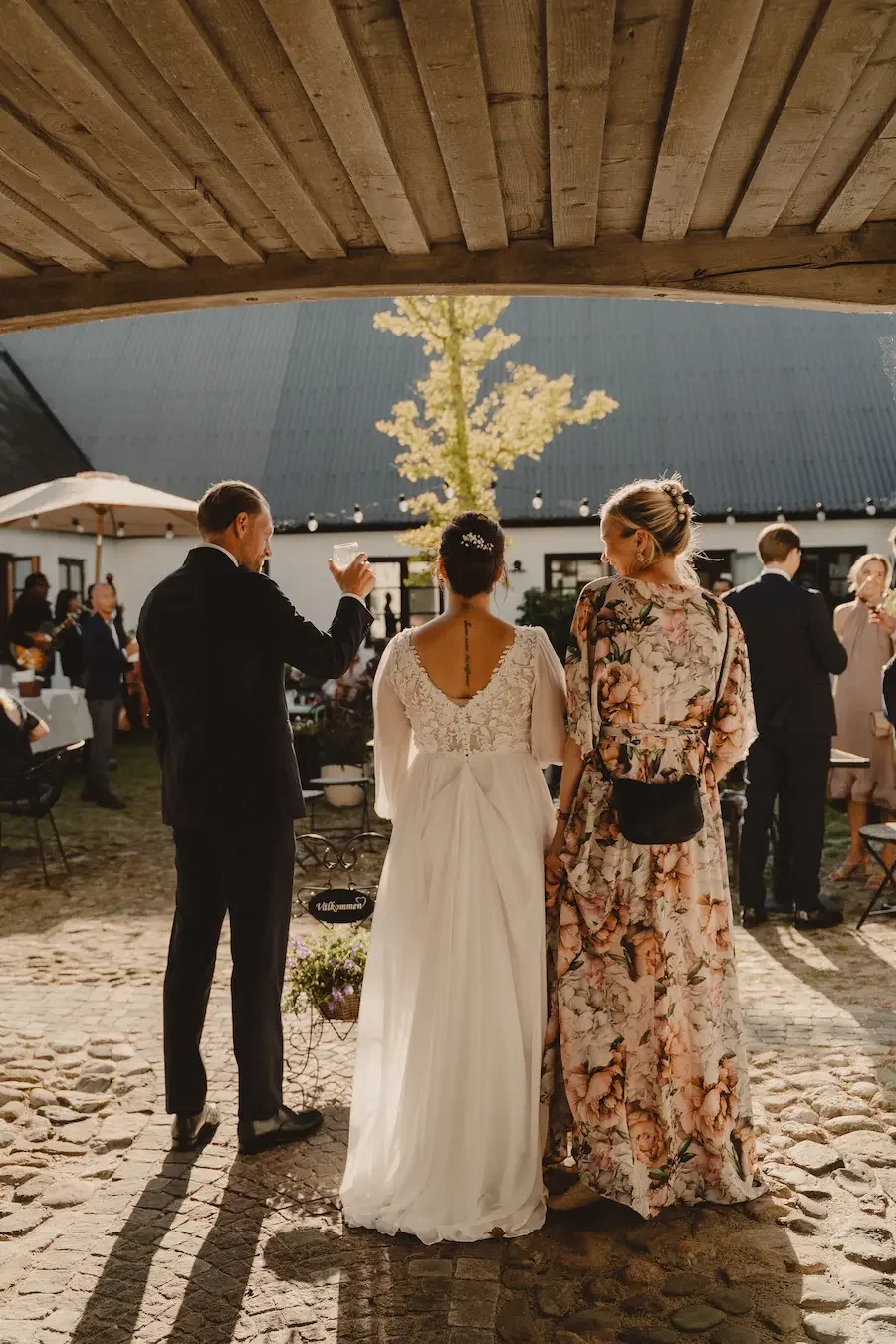 Brudparet skålar med en gäst under mingel utomhus på Mellby Atelier på Österlen. 