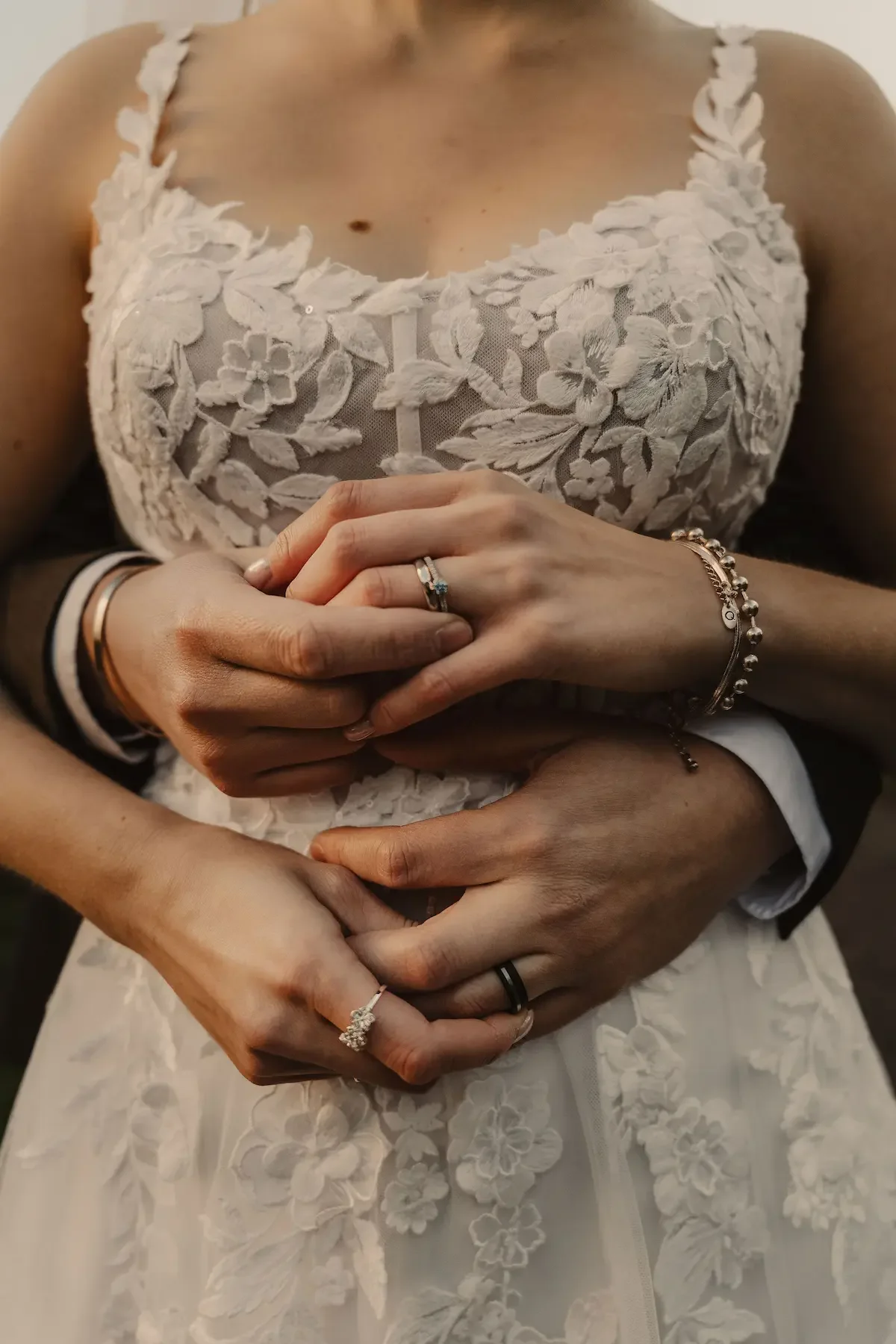 Kreativ närbild med editorial känsla av ett elegant brudpar som kramas, där händerna och vigselringarna är i fokus.