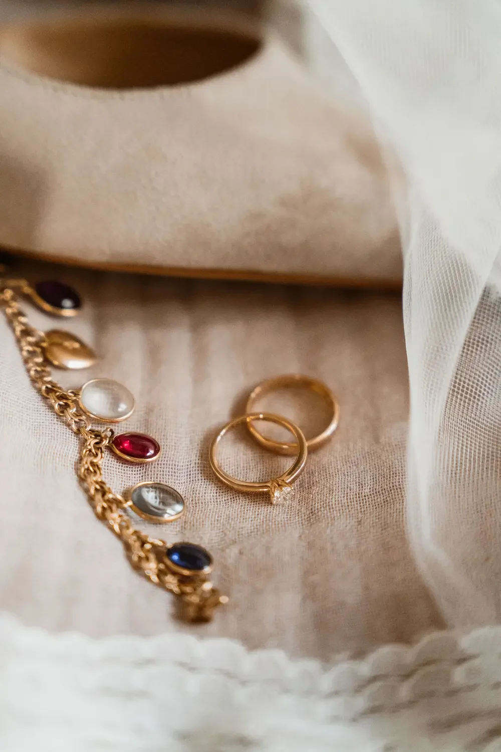 Romantisk och editorial detaljbild av ringar och brudsmycken med slöja och skor i bakgrunden. 