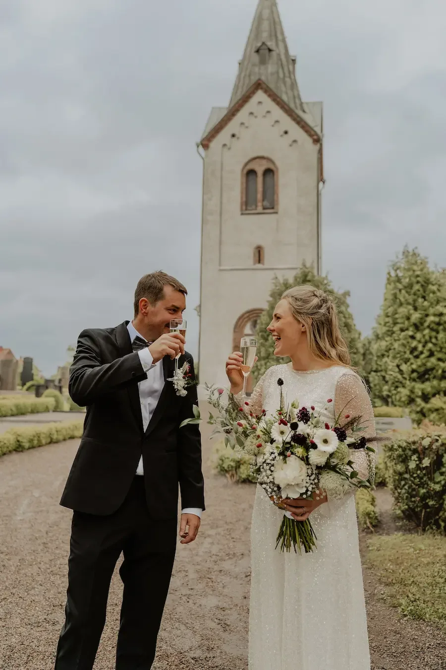 Brudpar skålar efter sin vigsel utanför gammal skånsk kyrka i Staffanstorp.