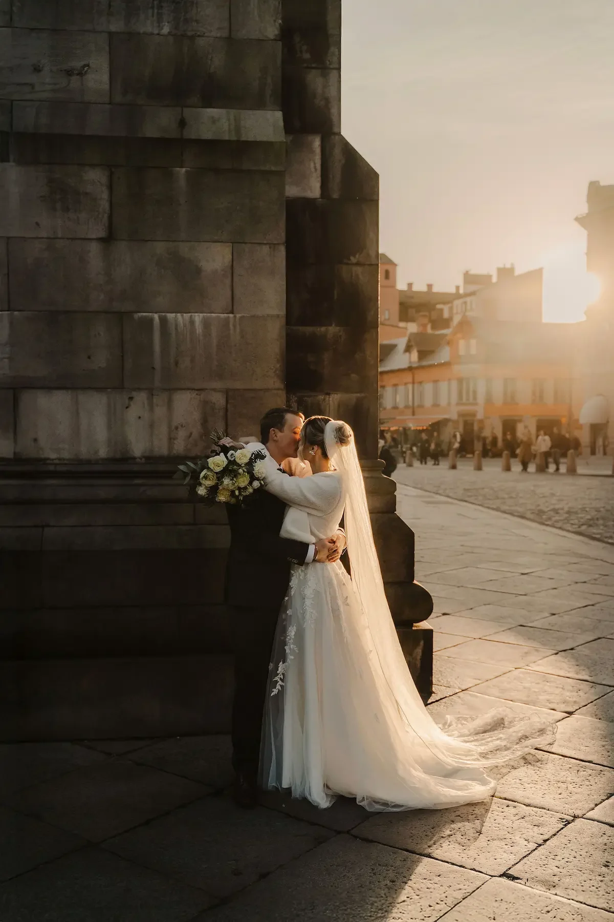 Brudpar kysser varandra utanför Lunds domkyrka under golden hour på ett soligt vinterbröllop, med mjuk, filmisk känsla. 