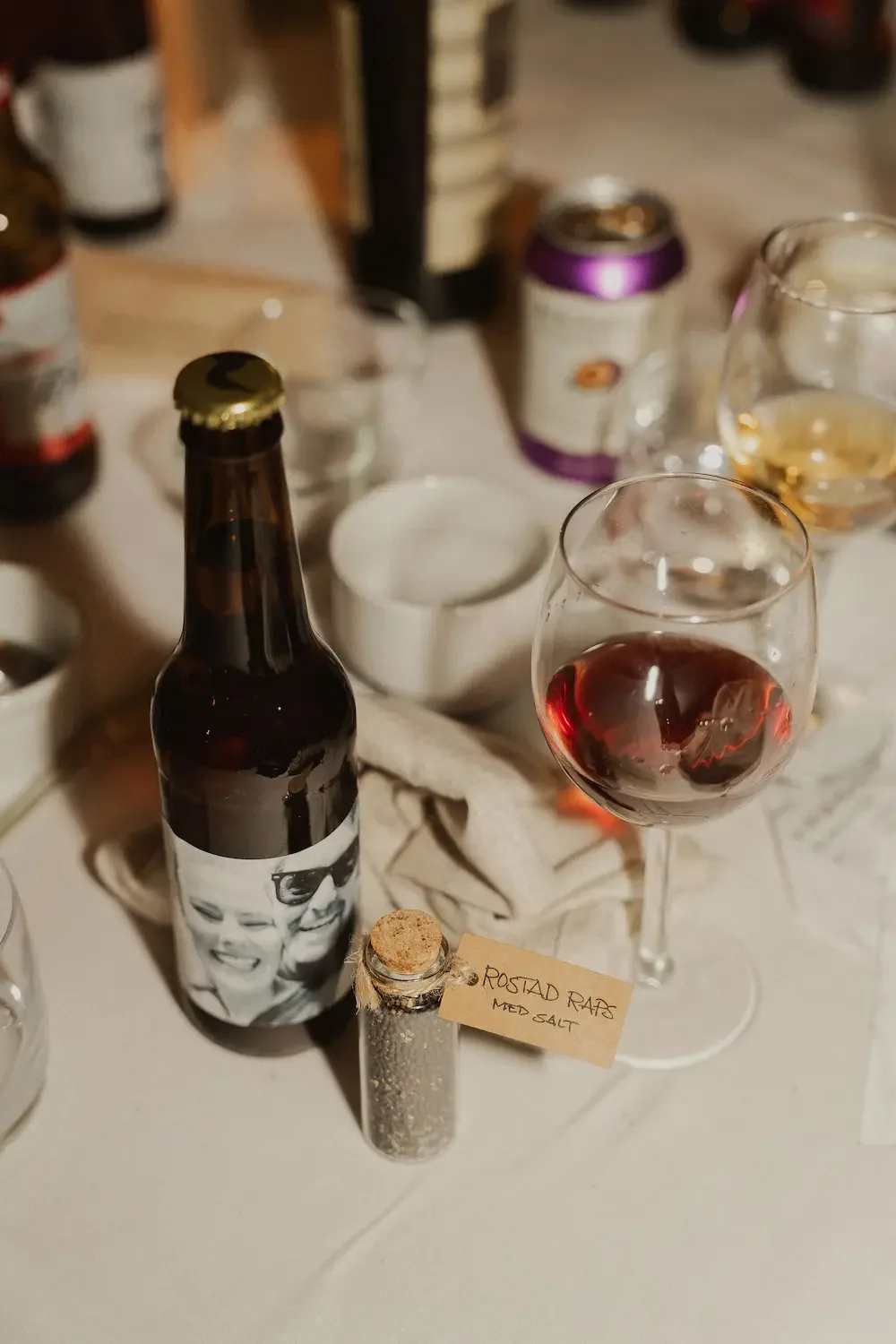 Närbild av estetiskt stök på ett bröllopsbord, med personliga detaljer som bordsgåvor och öl med specialdesignade etiketter