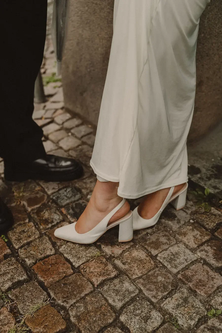 Närbild på brudens klackar som står på blöt kullersten i Göteborg under ett bröllop med regn.