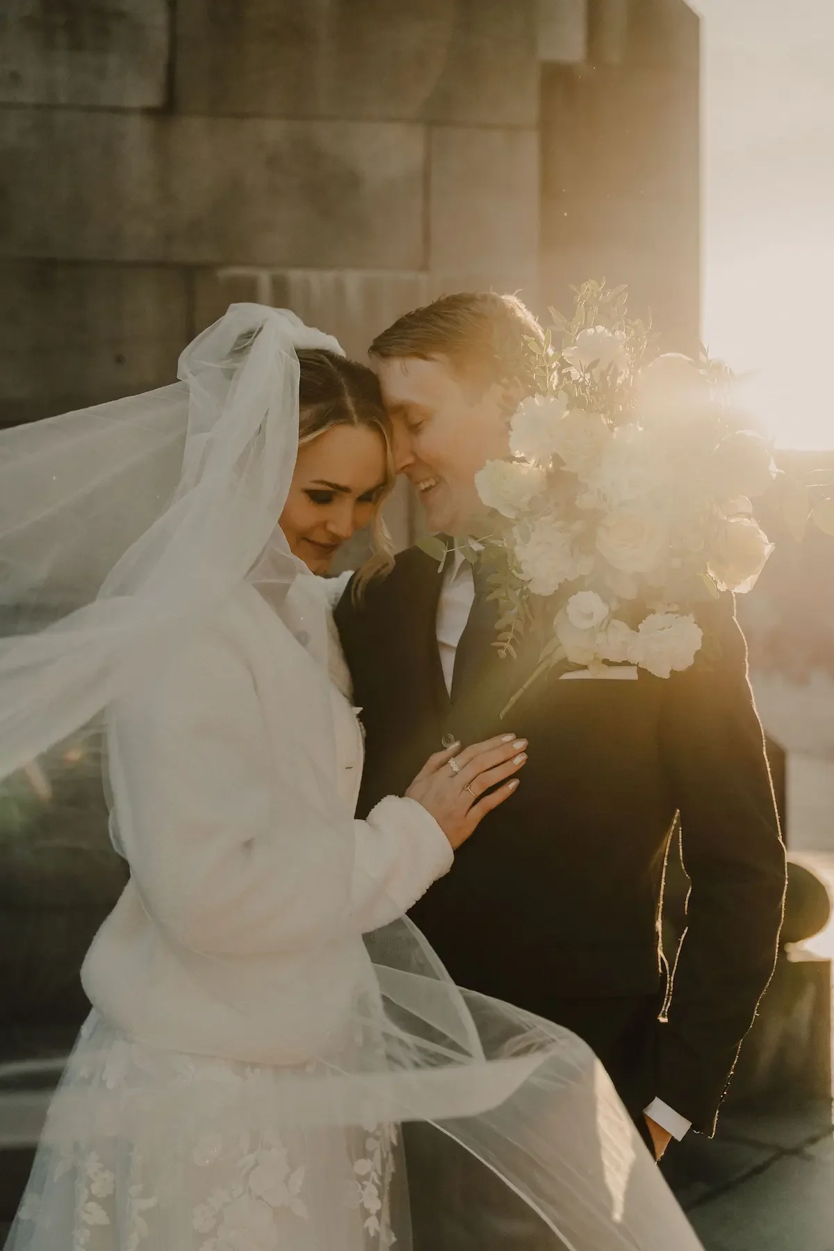Brudpar som lutar huvudena mot varandra under solig bröllopsfotografering på vintern utanför domkyrkan i Lund.