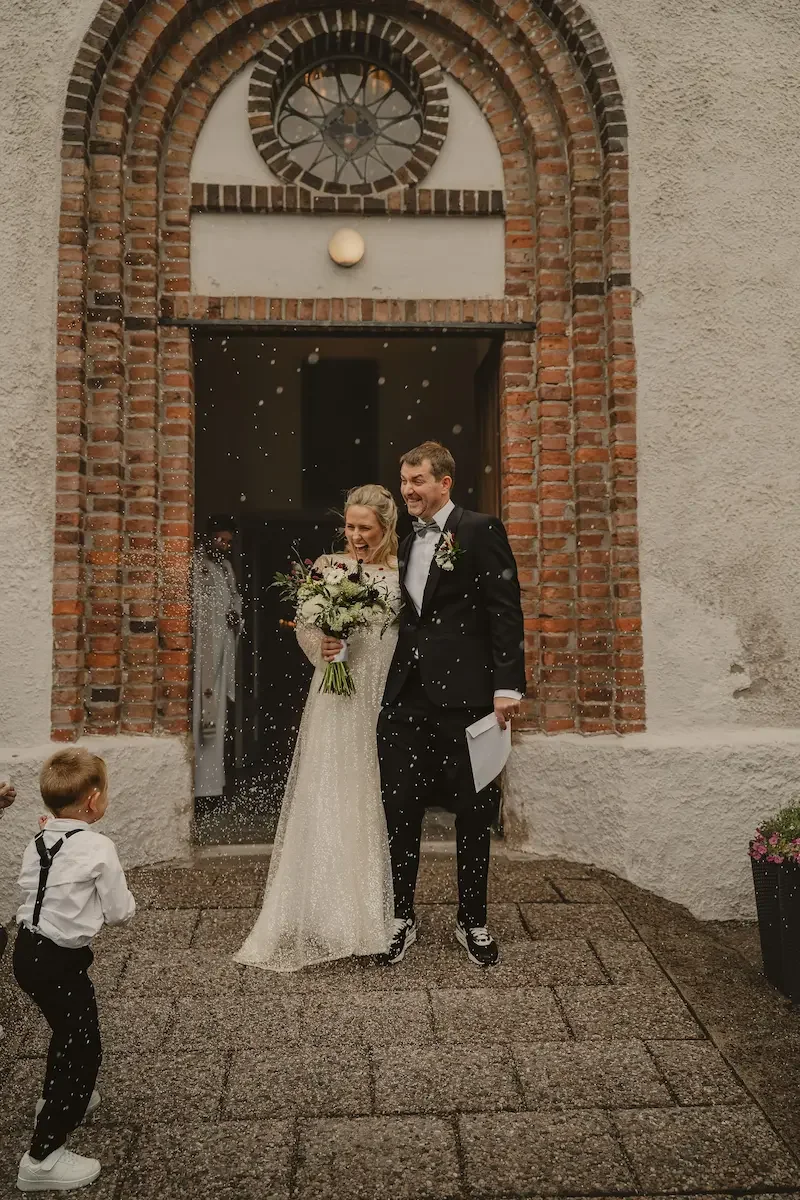 Ett barn kastar ris på ett glatt brudpar utanför Kyrkheddinge Kyrka i Skåne. 
