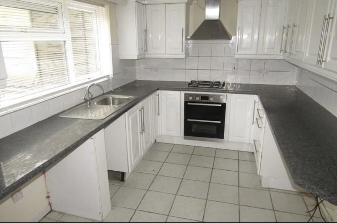 Kitchen with white cabinets, black countertops, a window with blinds, a sink, and a stove with an oven.