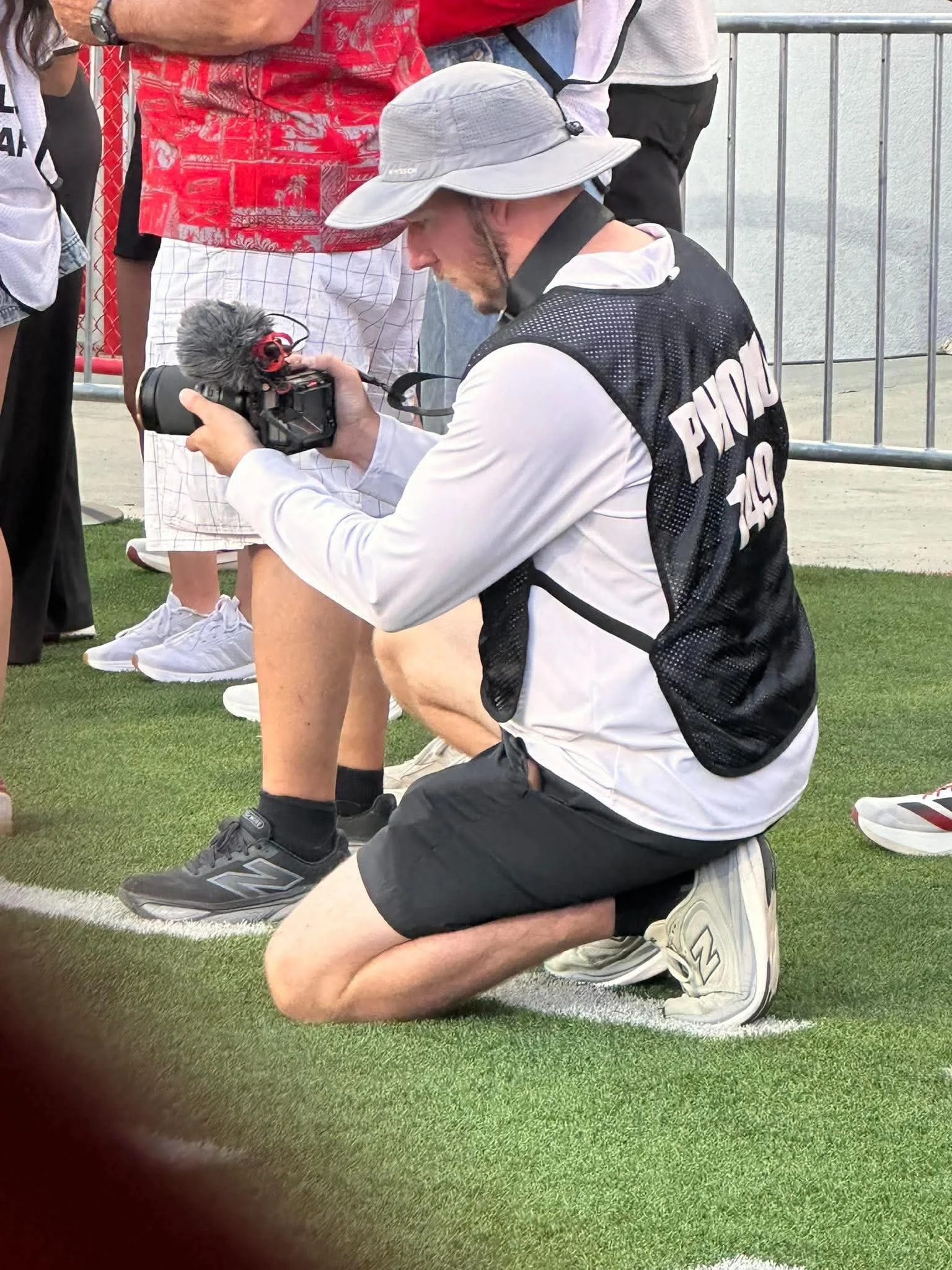 Dylan kneeling with a camera while filming from a football sideline.
