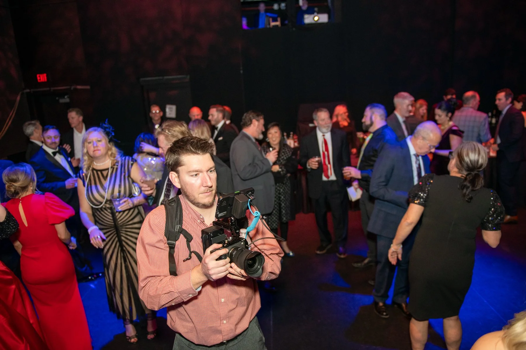 Videographer holding a camera among guests at an evening event.