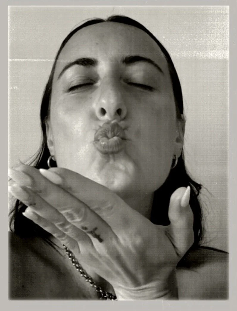 Mujer con ojos cerrados, labios en forma de beso, tocando su barbilla con mano, usando una cadena y pendientes.