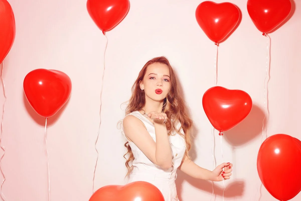 Woman in white dress blowing a kiss holding red balloons