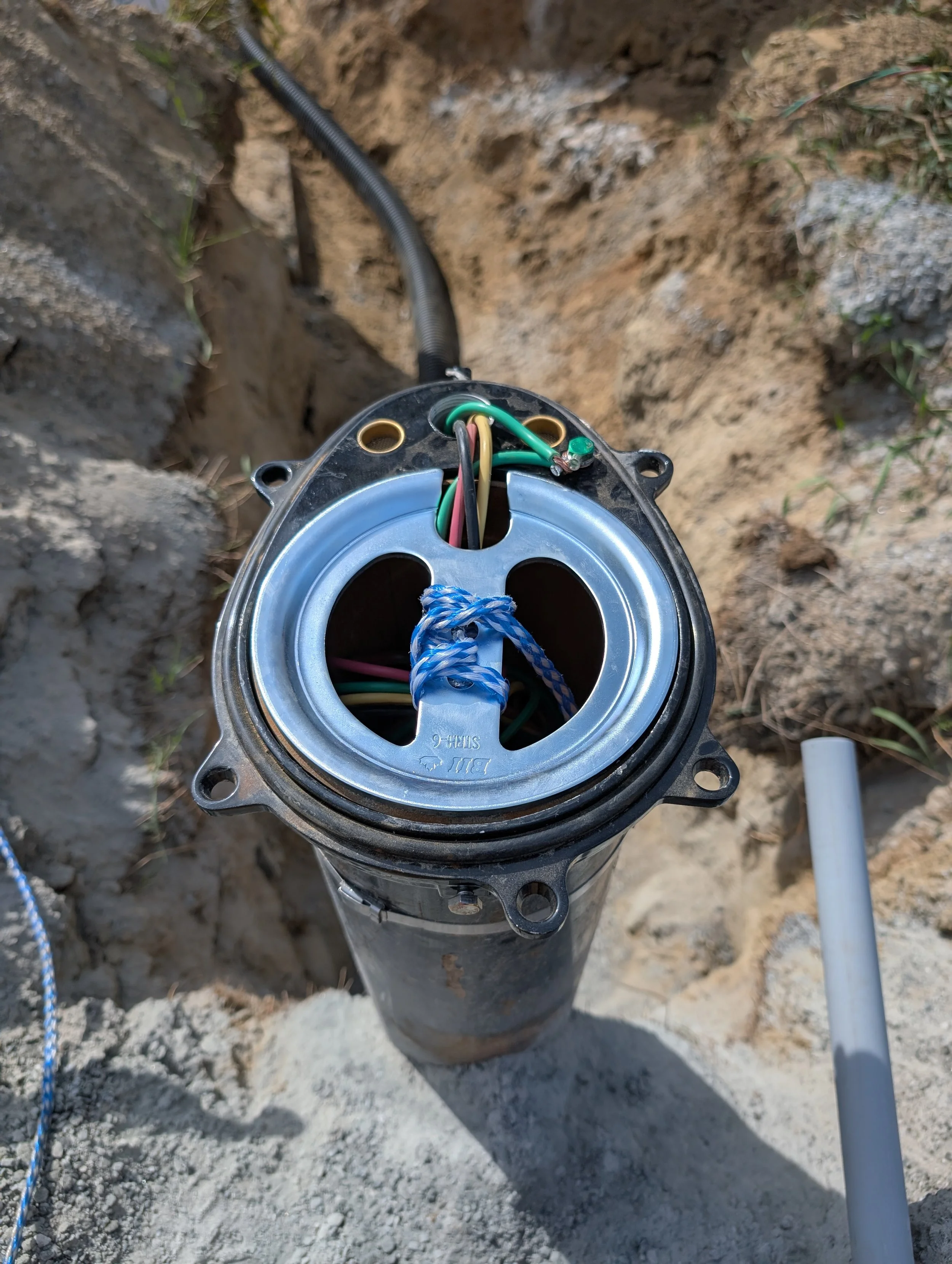 An underground electrical junction box with multiple wires connected, installed in a dug hole in the ground.