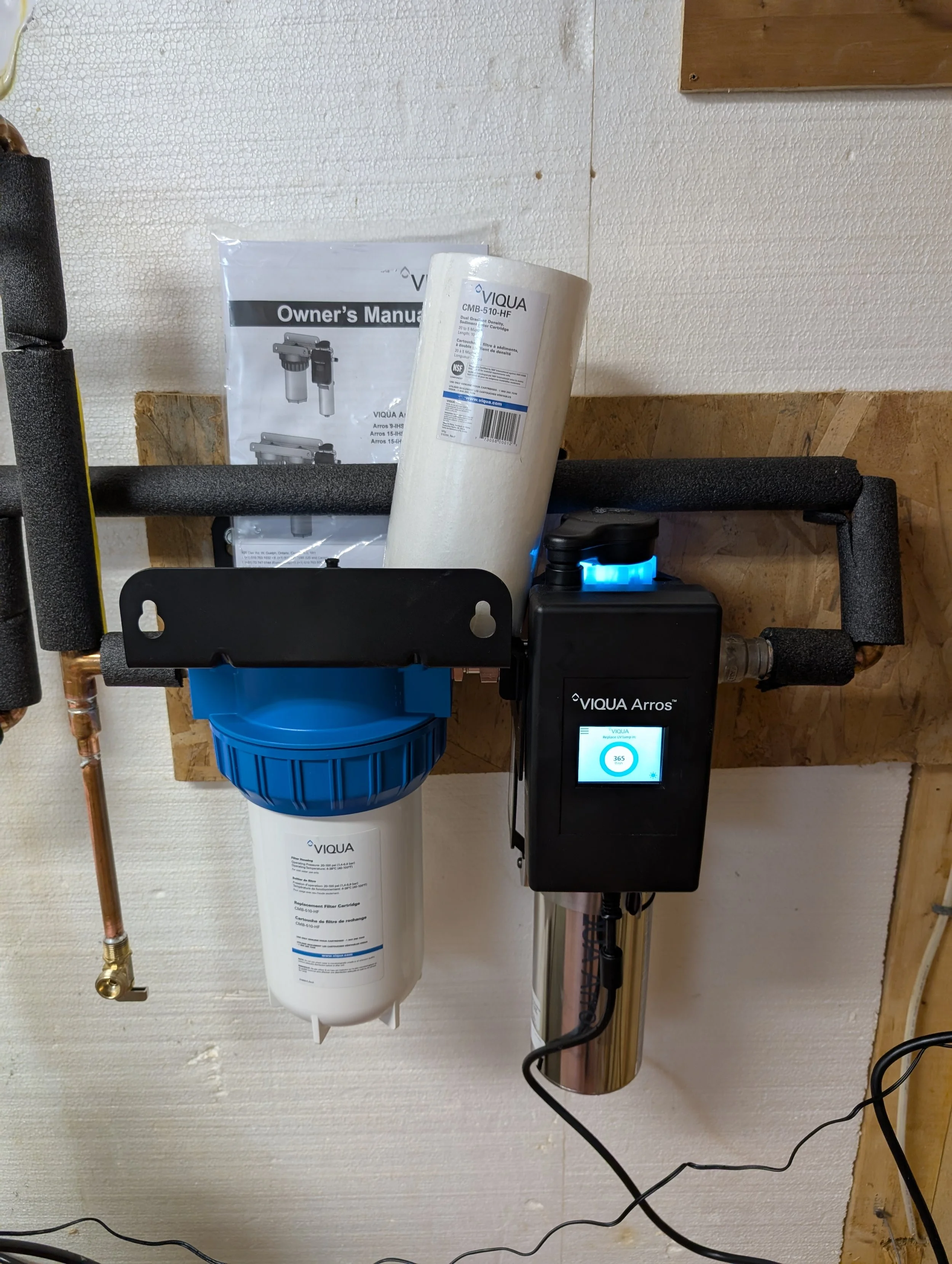 Water filtration system with a filter cartridge, digital control unit, and pipes mounted on a wall.