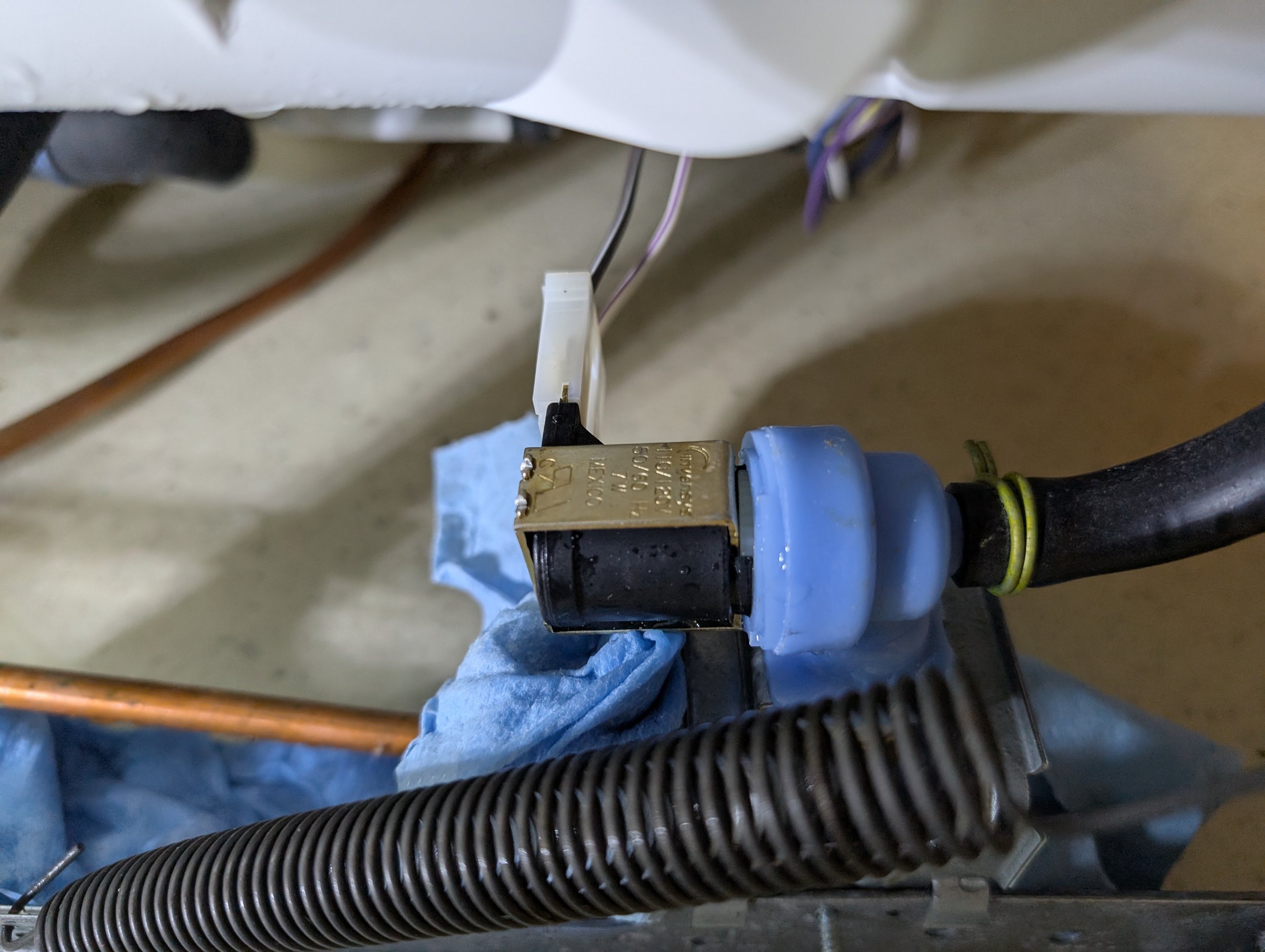 Close-up of a plumbing setup with black hoses, a brass valve, and some electrical wiring, underneath a white surface.