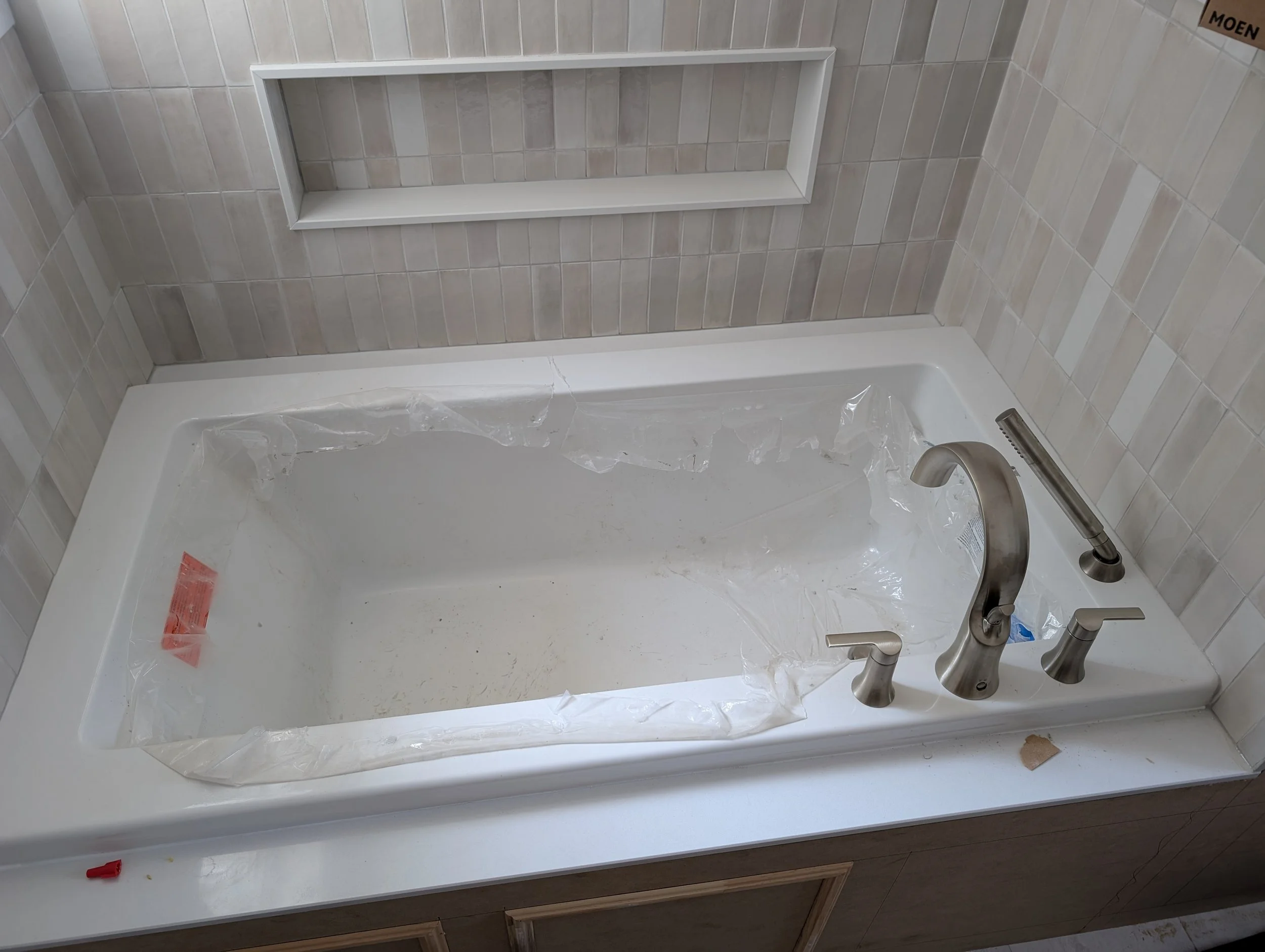 Bathroom vanity with a white sink, a modern faucet, and a tiled wall in the background. Part of a cabinet with a wood finish is visible at the bottom.