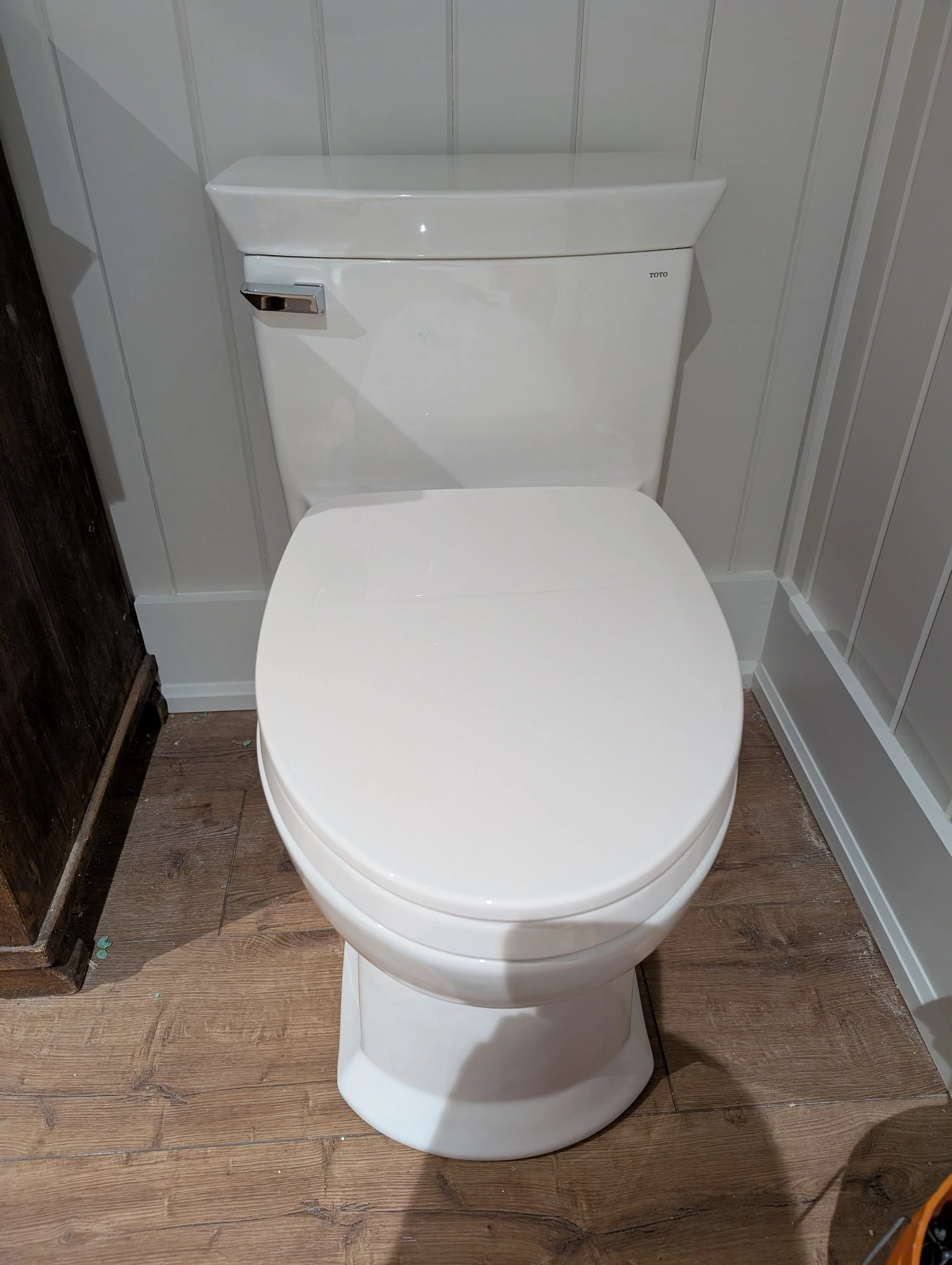 A white toilet with a tank and a wooden floor in a bathroom.