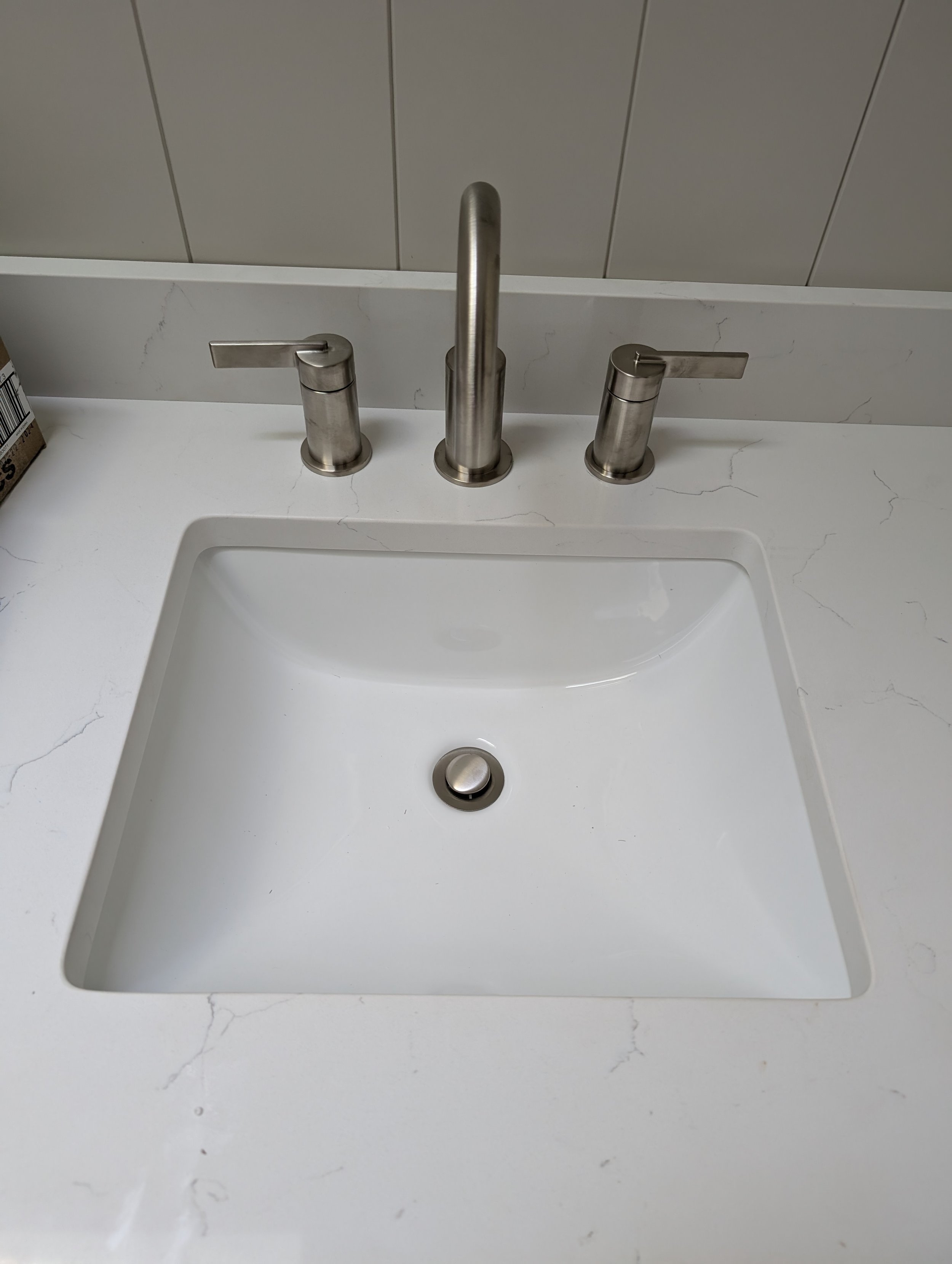 A modern bathroom sink with a white marble countertop, three stainless steel faucets, and a background of beige tiled wall.