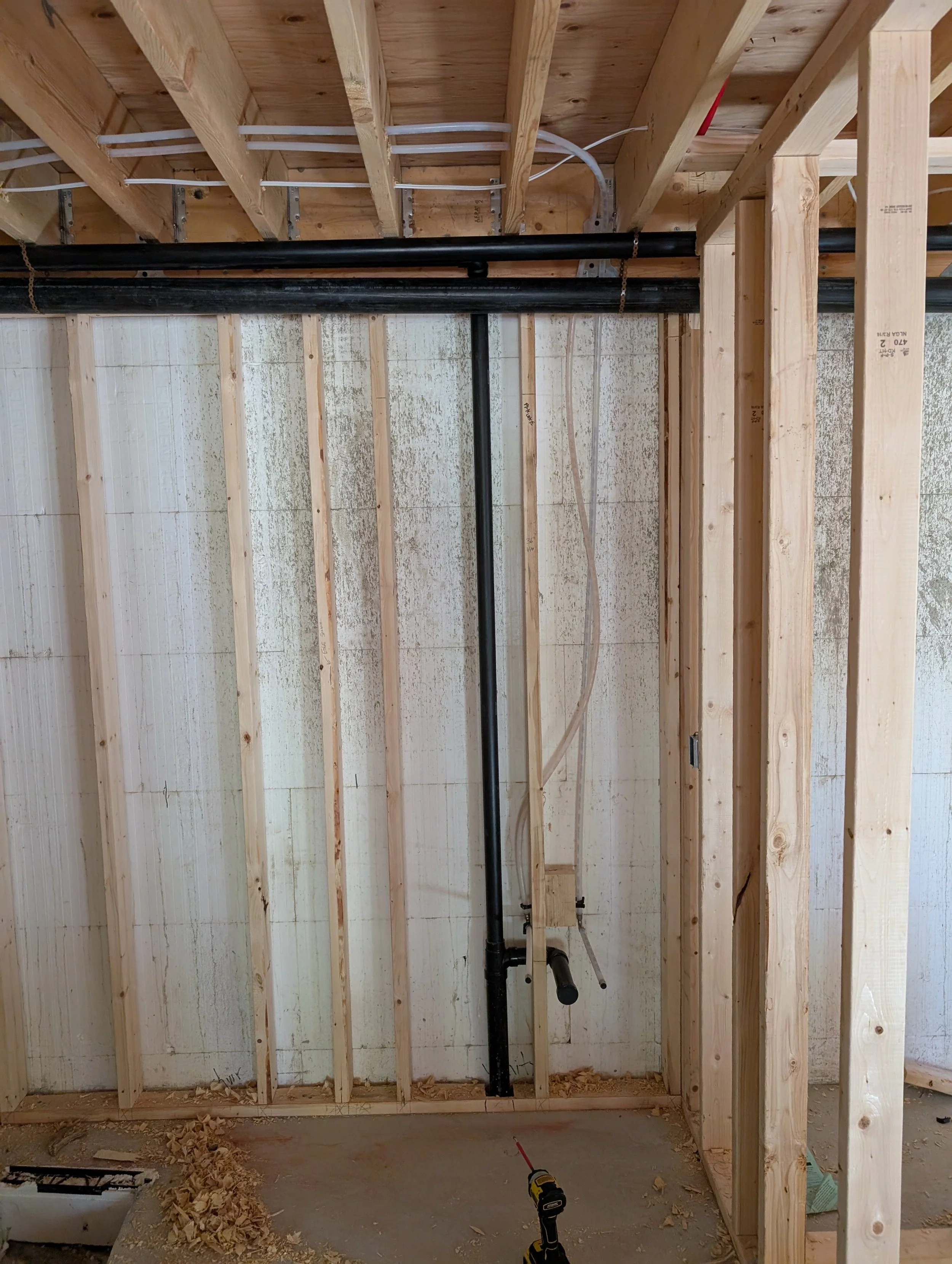 Construction site with exposed wooden framing and plumbing pipes, unfinished interior.