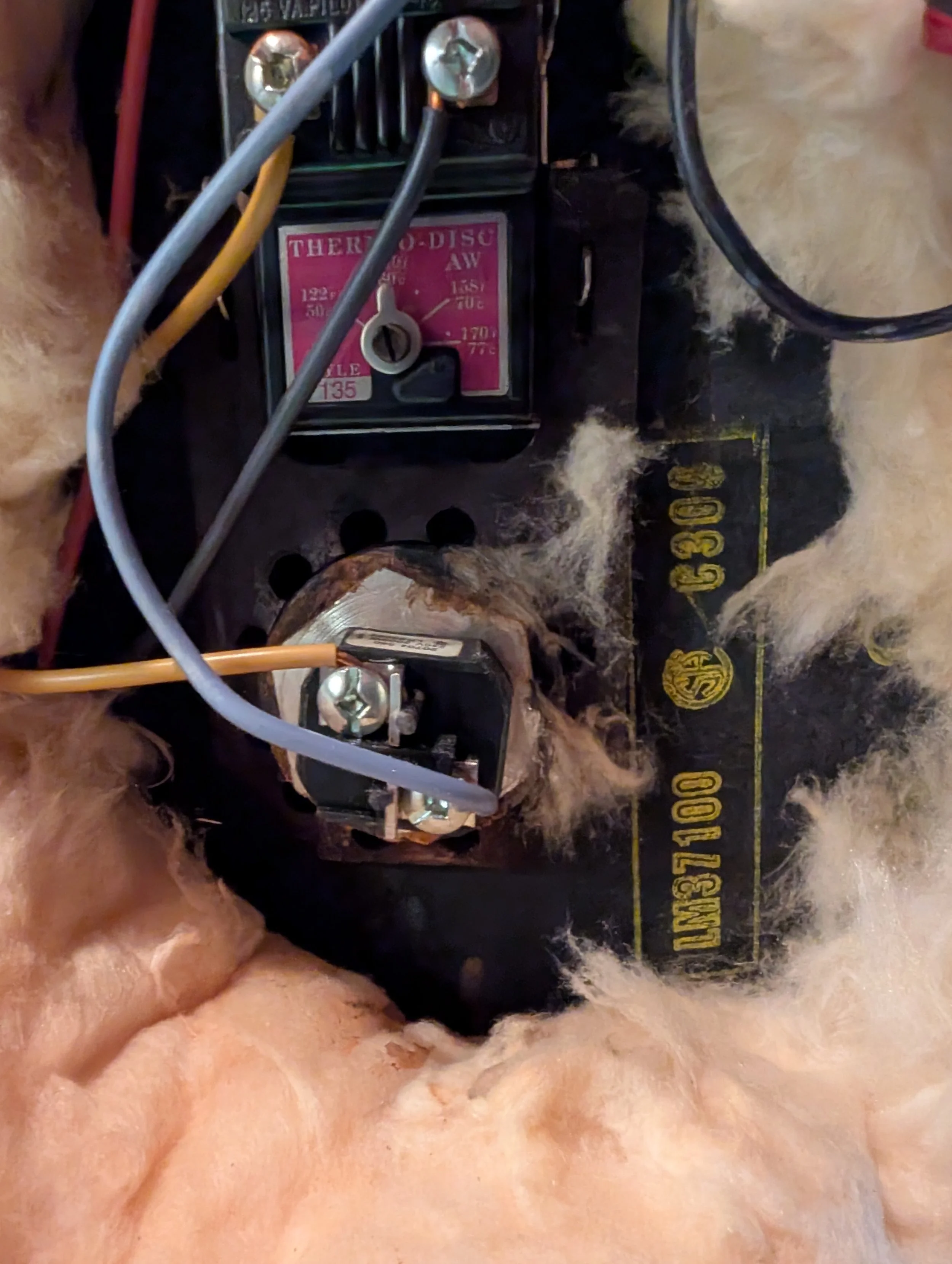 Close-up of electrical components and wires connected to a black device mounted on a surface with an orange furry material nearby.