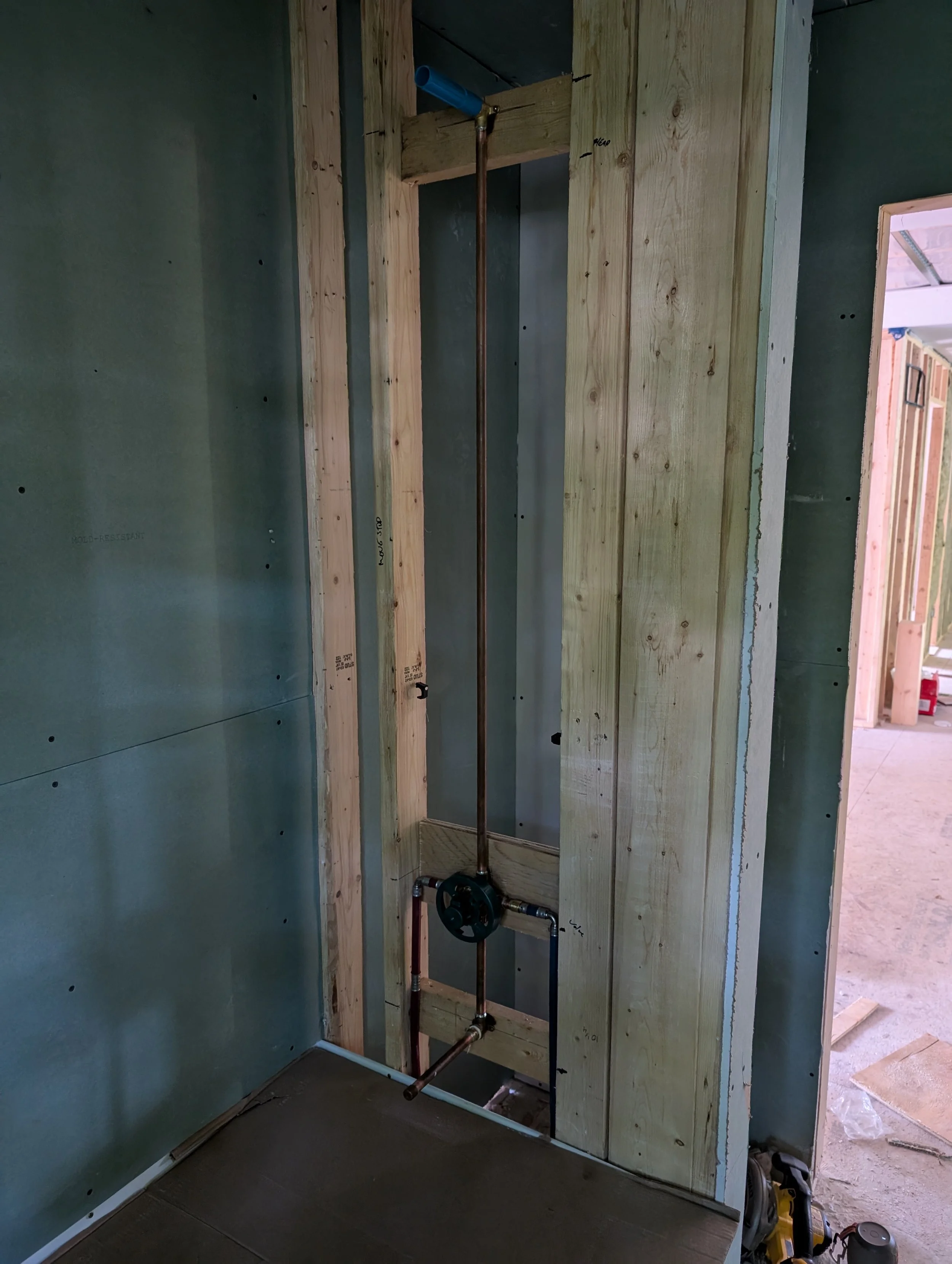 Construction site with unfinished wooden framing and plumbing pipes, in a room under renovation.