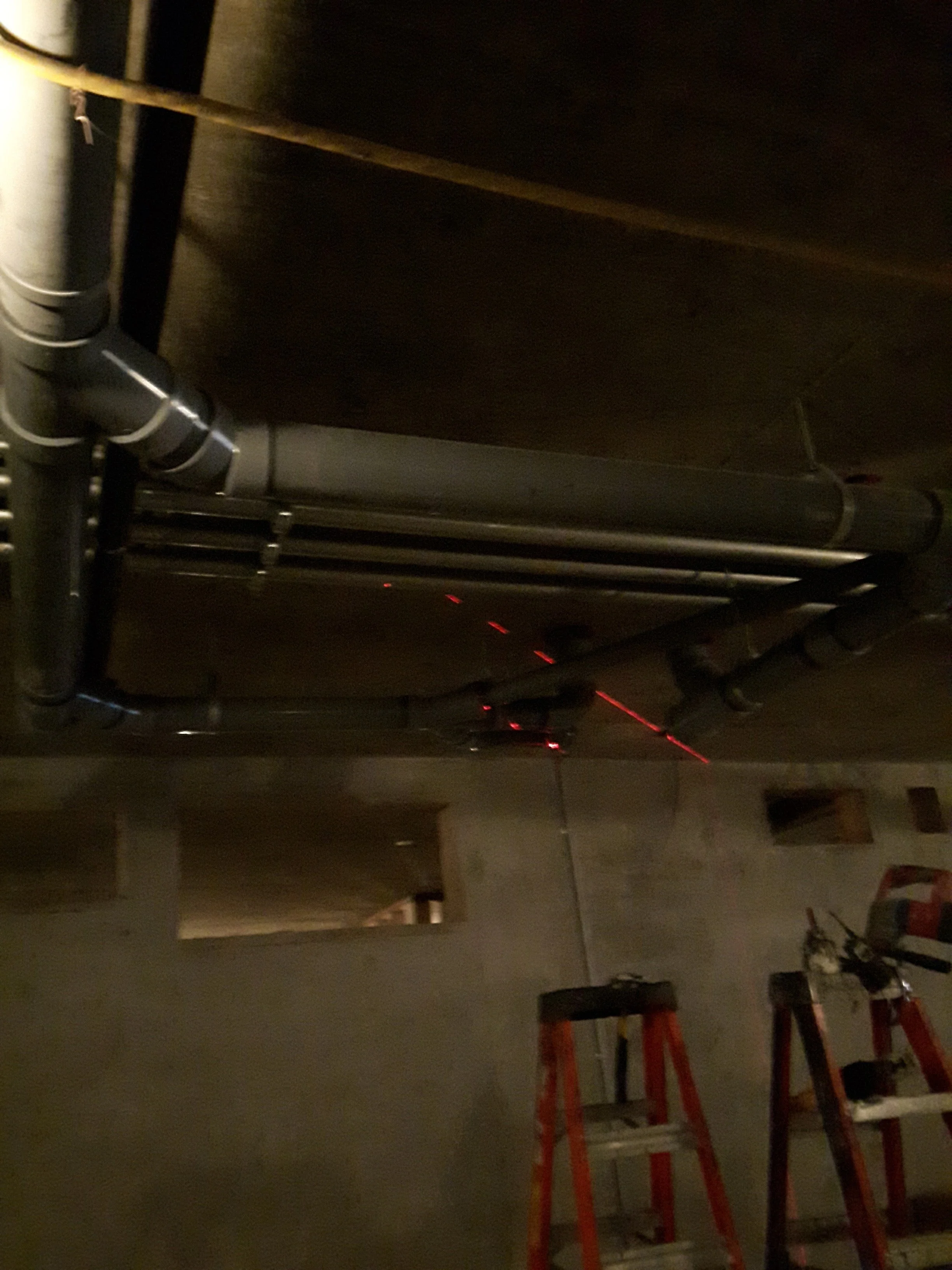 Image of a dark room or garage with several ladders and some equipment, including a black rolling cart or platform and red ladders, with a dimly lit background.