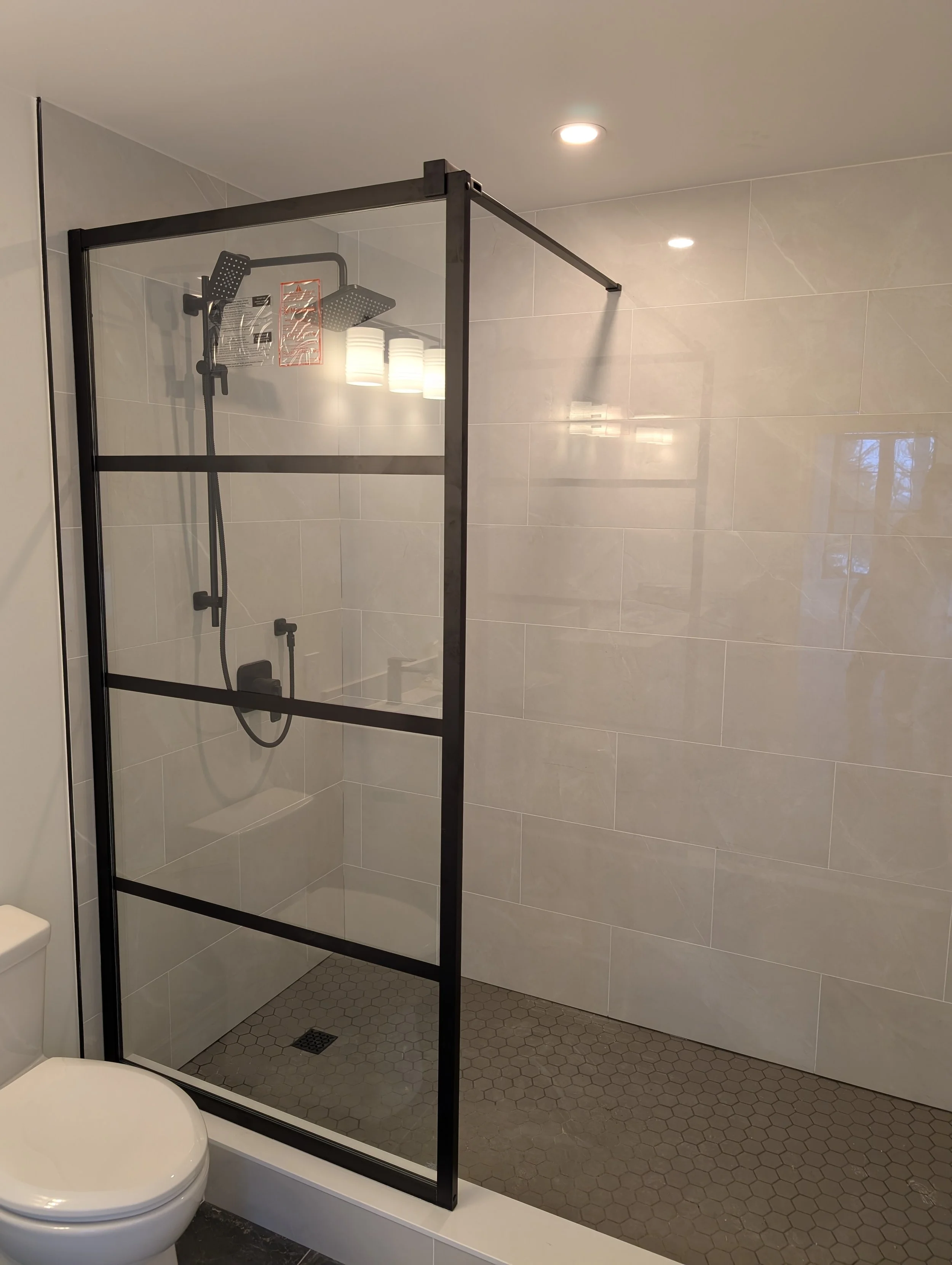Modern bathroom with a glass shower enclosure, white tiled walls, and hexagonal tile flooring.