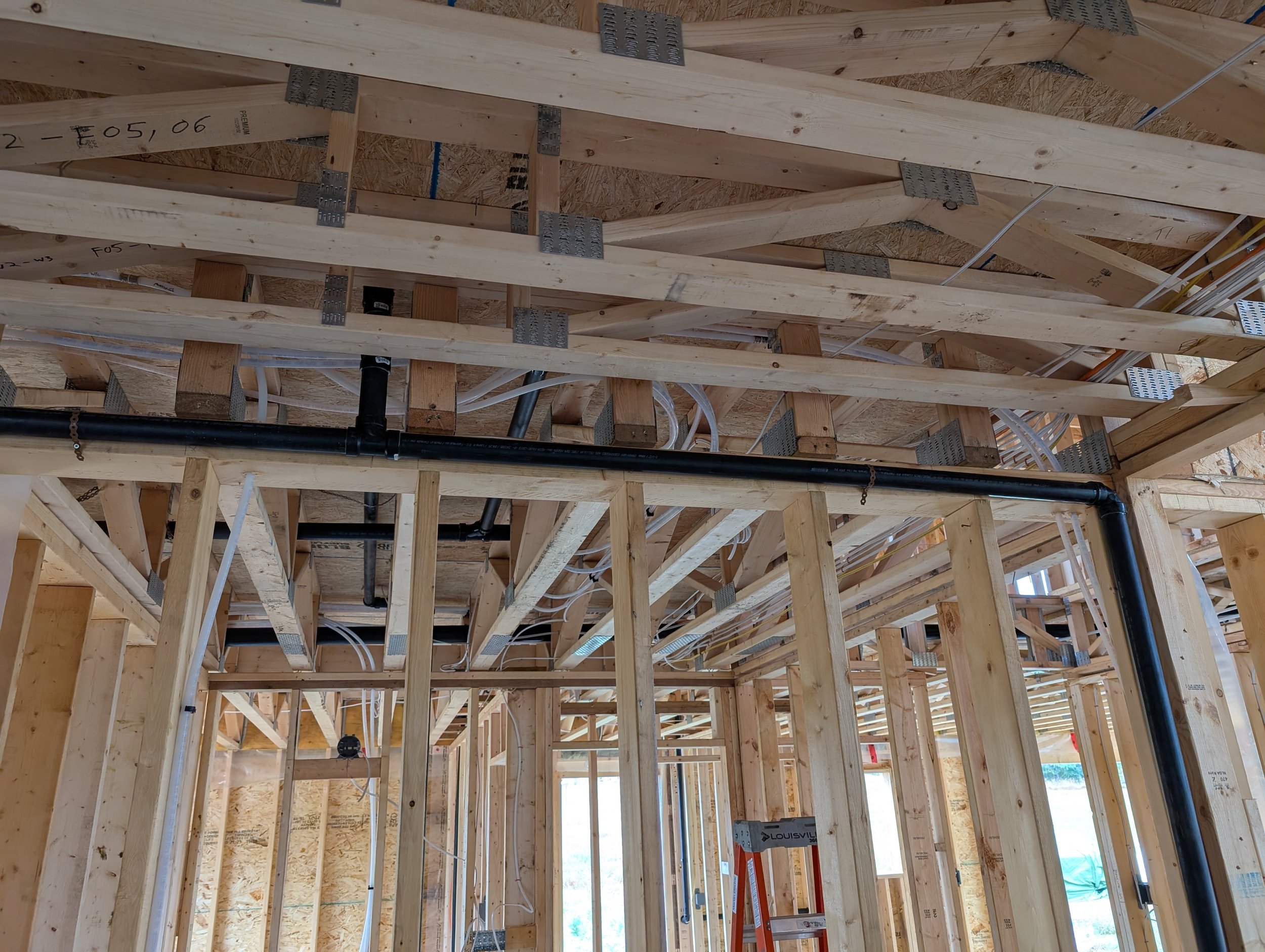 The image shows the interior wooden framework of a building under construction, including wooden beams, electrical wiring, and metal brackets.